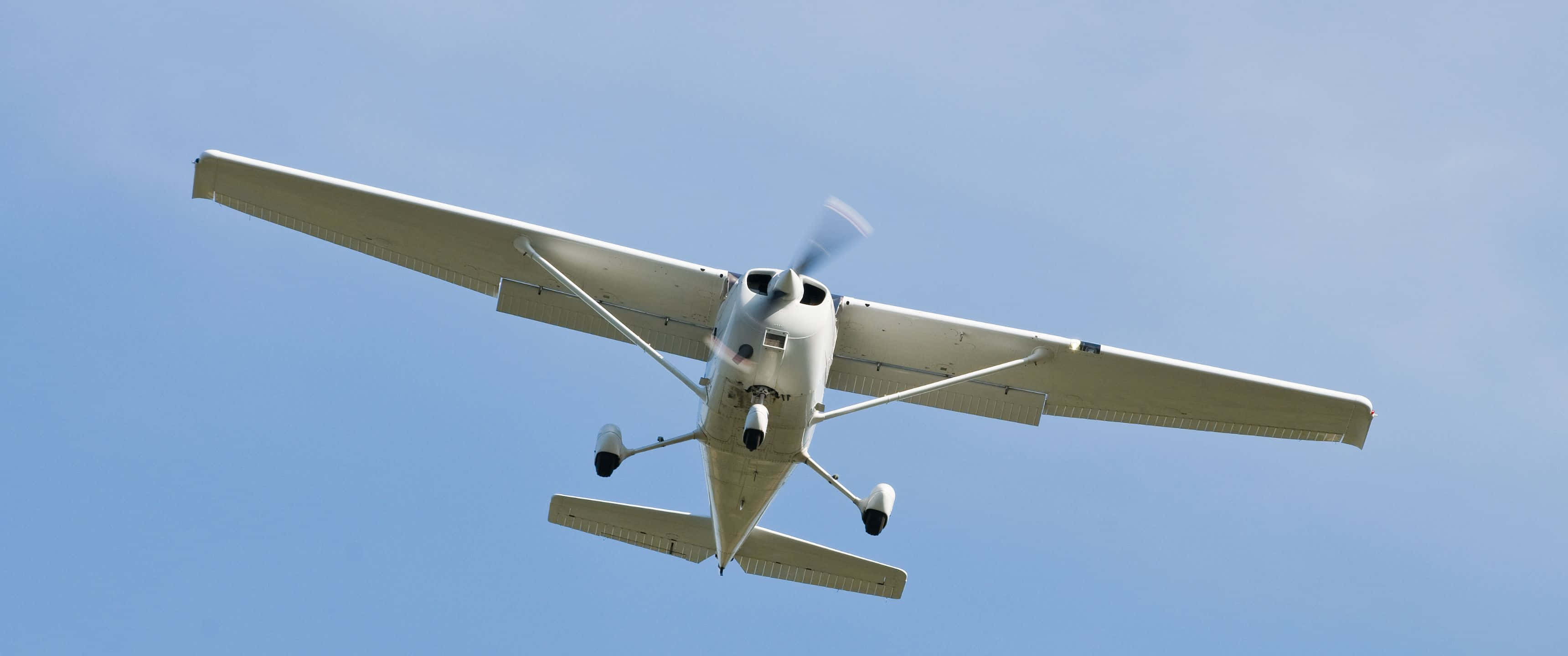 3440x1440p Small Planes 桌布 壁紙 — 一架白色單引擎螺旋槳飛機在晴朗的藍天下飛過頭頂，起落架放下。