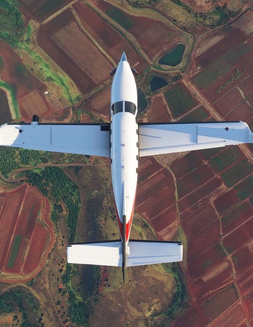 Android Microsoft Flight Simulator 桌布 壁紙 — 一架白色單引擎飛機飛過由紅褐色和綠色農田組成的拼布圖案上空。