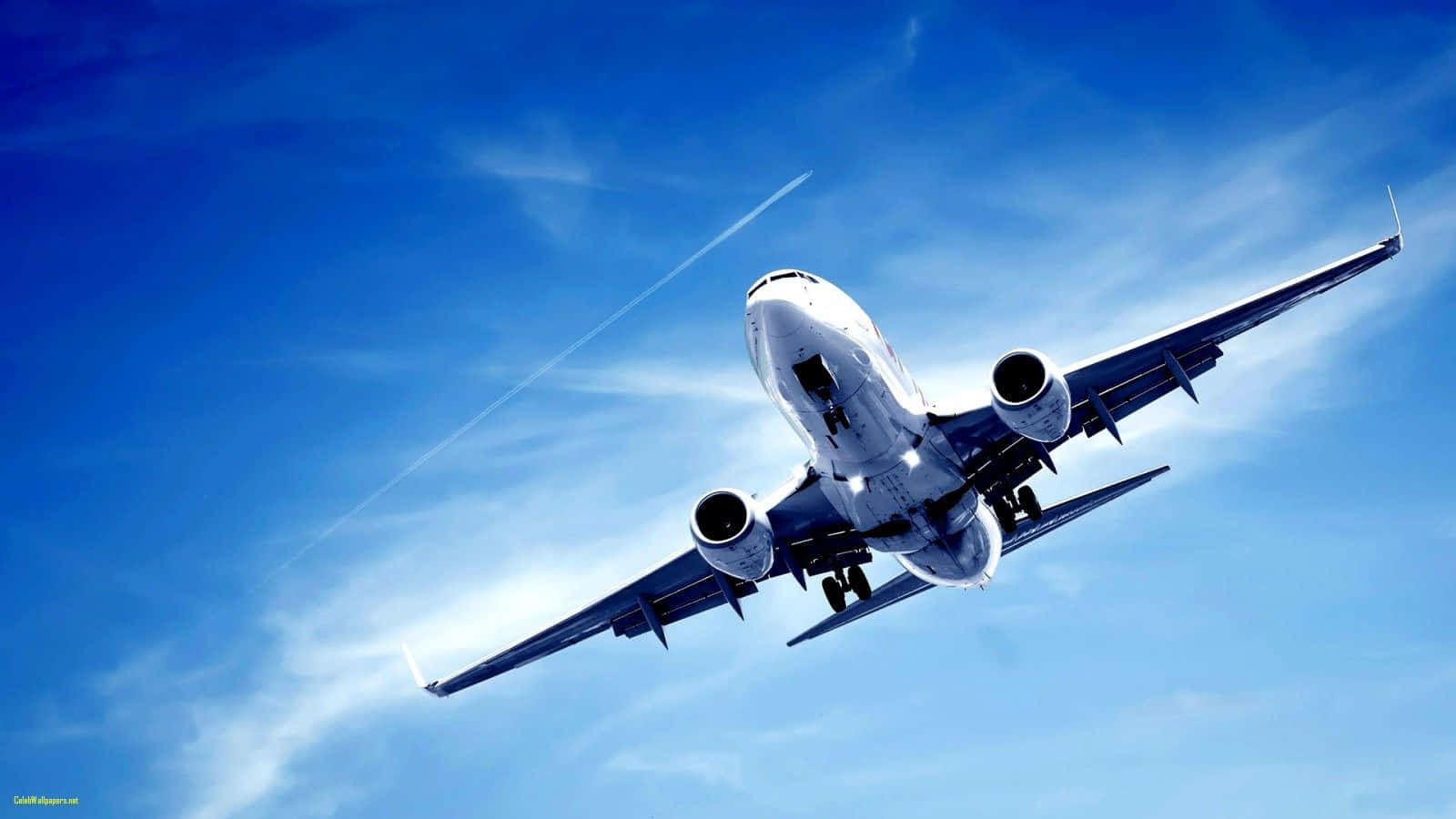 Jet 桌布 壁紙 — 一架白色客機在佈滿薄雲和凝結尾跡的鮮豔藍天中向上翱翔。