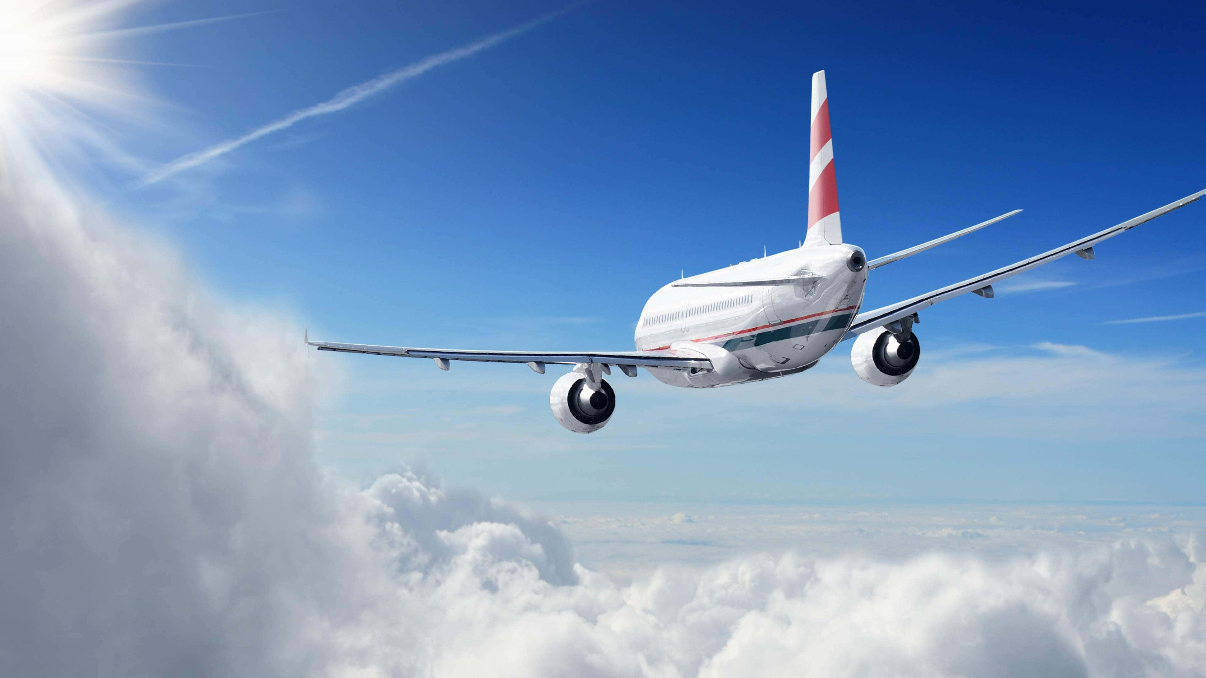 Plane 桌布 壁紙 — 一架白色客機在左上角陽光照耀的明亮藍天下，翱翔於蓬鬆的白雲之上。