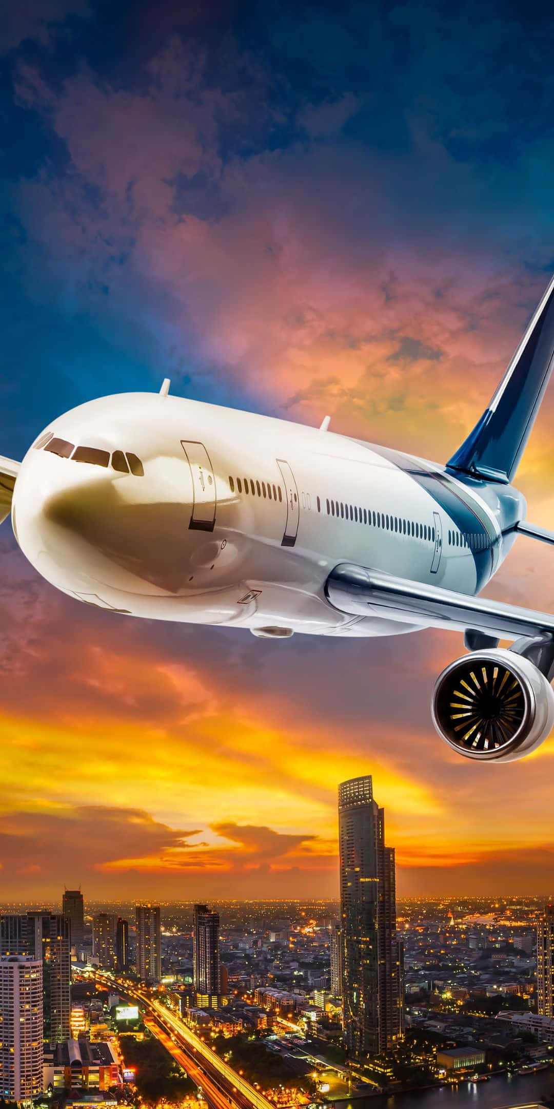 Pixel 3 Plane 桌布 壁紙 — 一架白色客機在日落時分翱翔於發光的城市天際線之上，下方是火紅的橙色雲朵和燈火通明的摩天大樓。