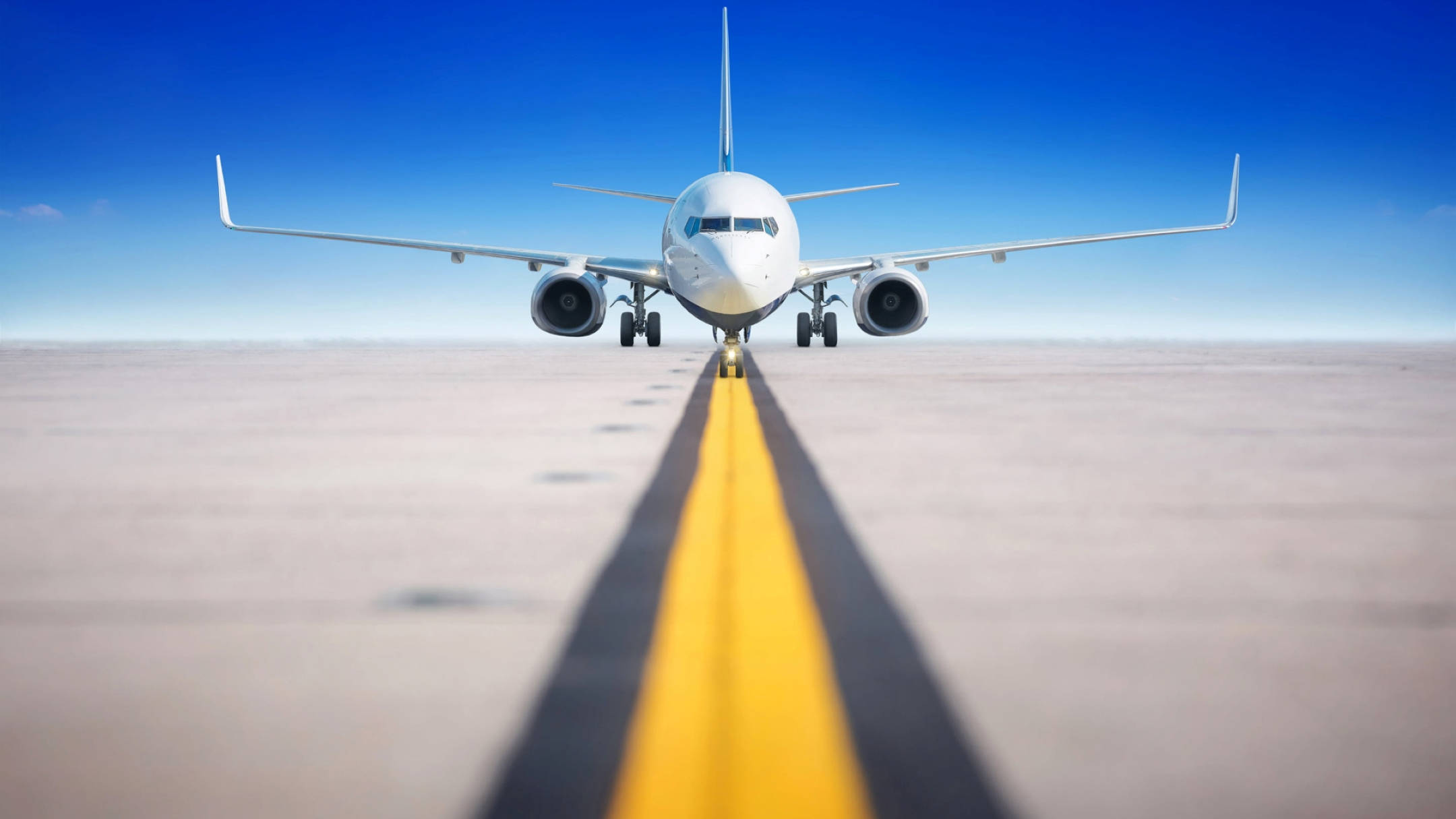 Runway 桌布 壁紙 — 一架白色客機在晴朗藍天下，面向跑道上的粗黃色中心線。
