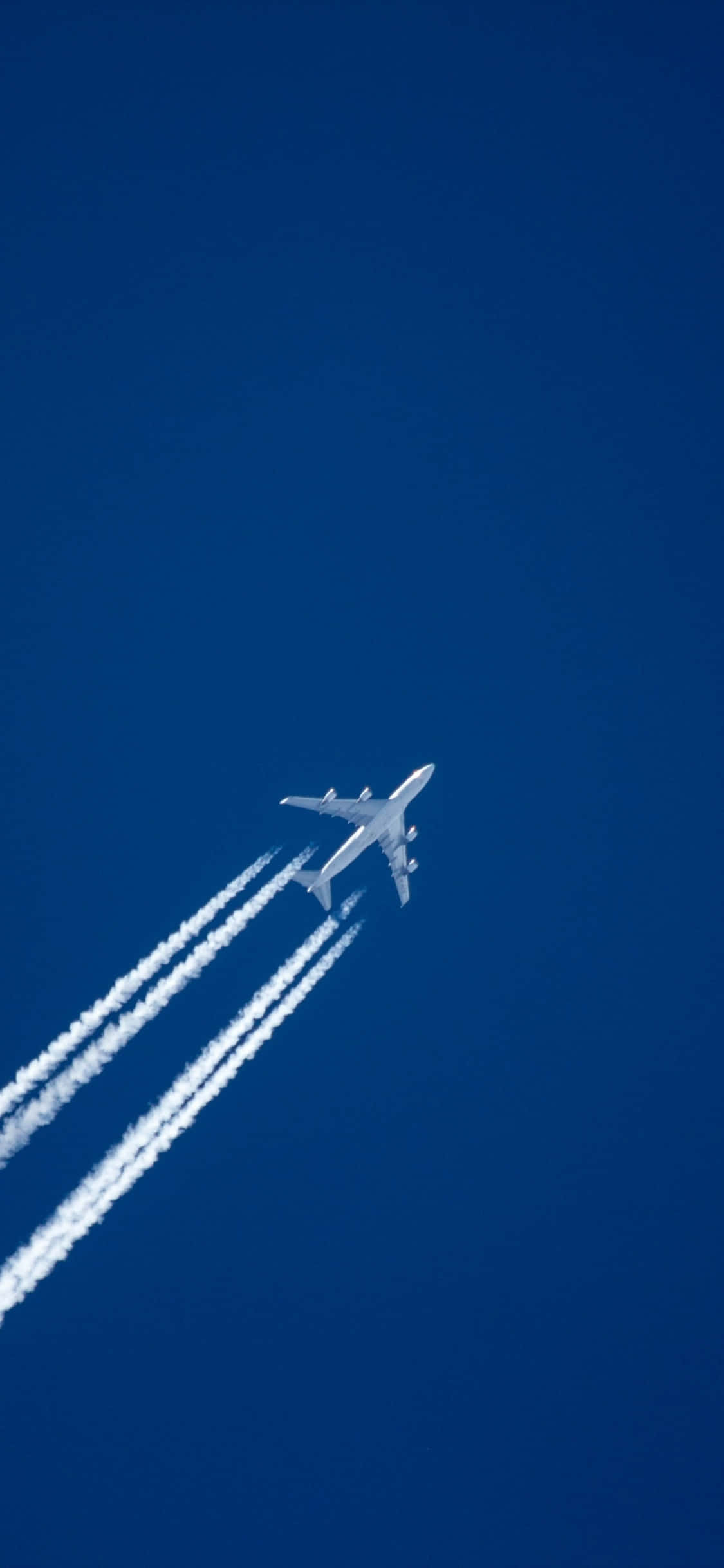 Flight 桌布 壁紙 — 一架白色客機在深藍色的天空中翱翔，身後留下三條清晰的白煙。
