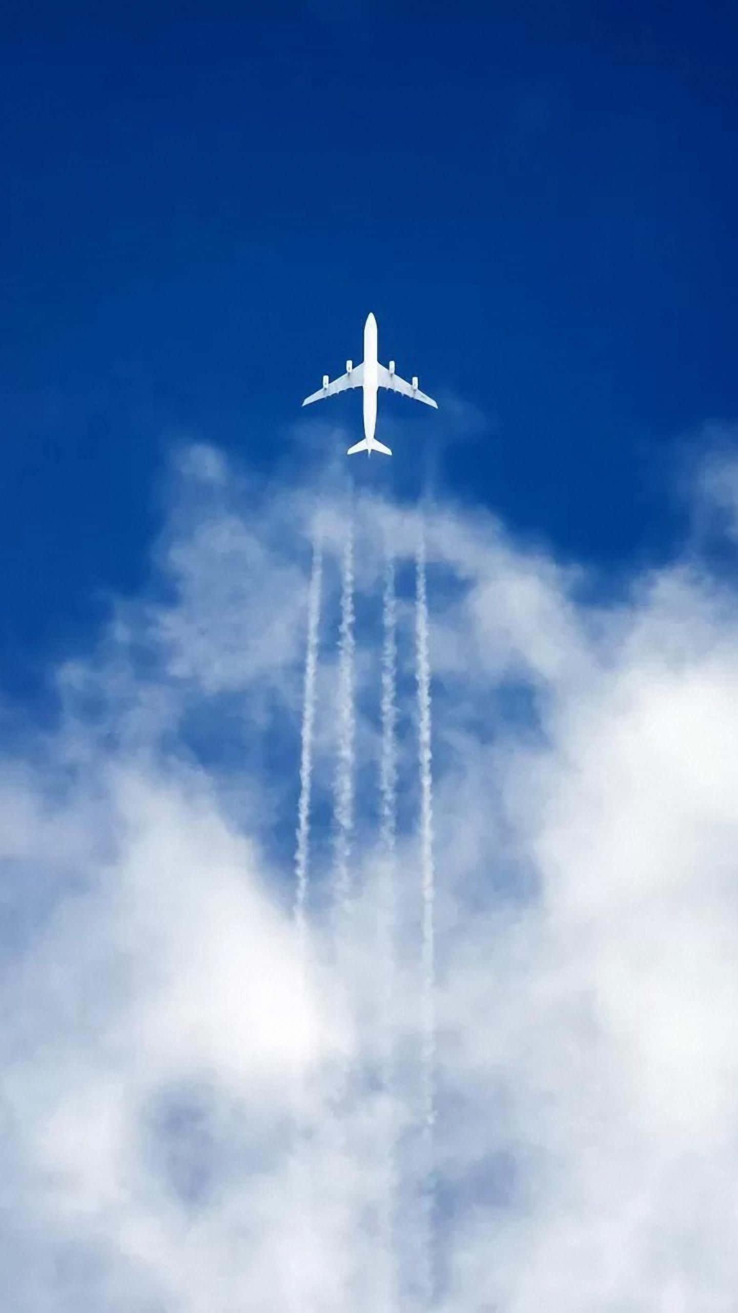 Plane 桌布 壁紙 — 一架白色客機在深藍色的天空中翱翔，飛過蓬鬆的白雲，留下四條明顯的凝結尾跡。