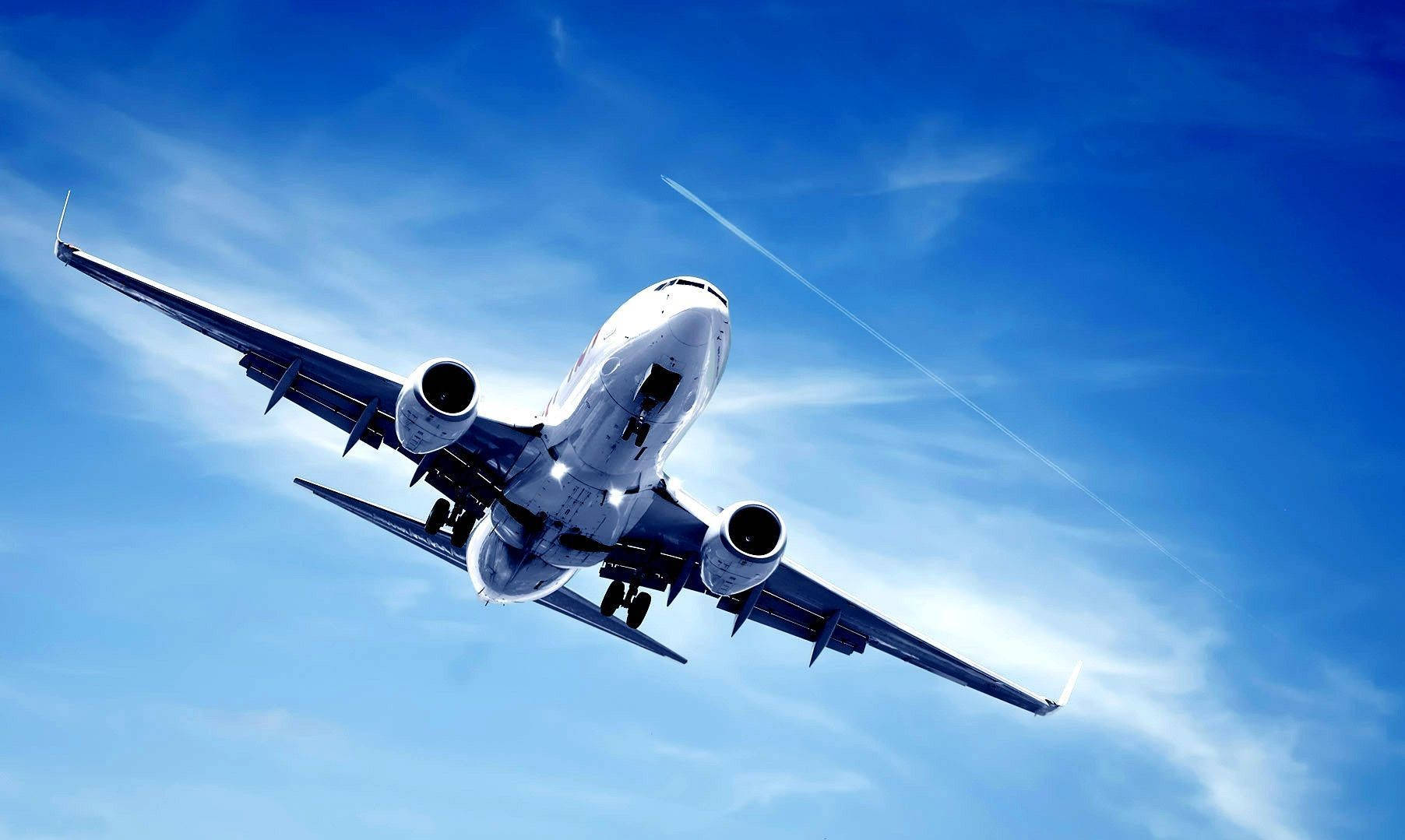 flying 桌布 壁紙 — 一架白色客機在蔚藍天空中向上翱翔，天空點綴著縷縷薄雲和淡淡的凝結尾跡。