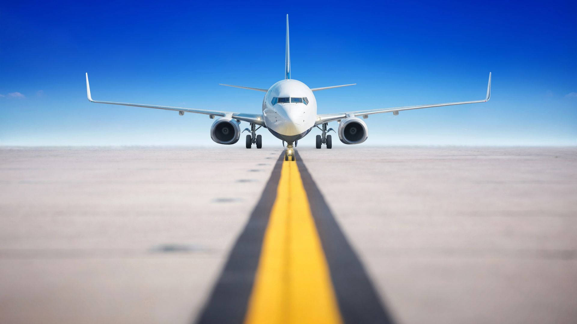 Runway 桌布 壁紙 — 一架白色客機在跑道上向前，跑道上有醒目的黃色中心線，天空清澈湛藍。