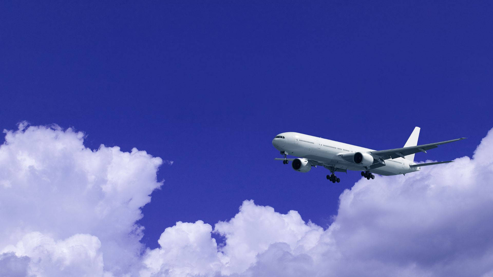 flying 桌布 壁紙 — 一架白色客機穿過蓬鬆的白雲，在湛藍的天空中下降，起落架已放下。