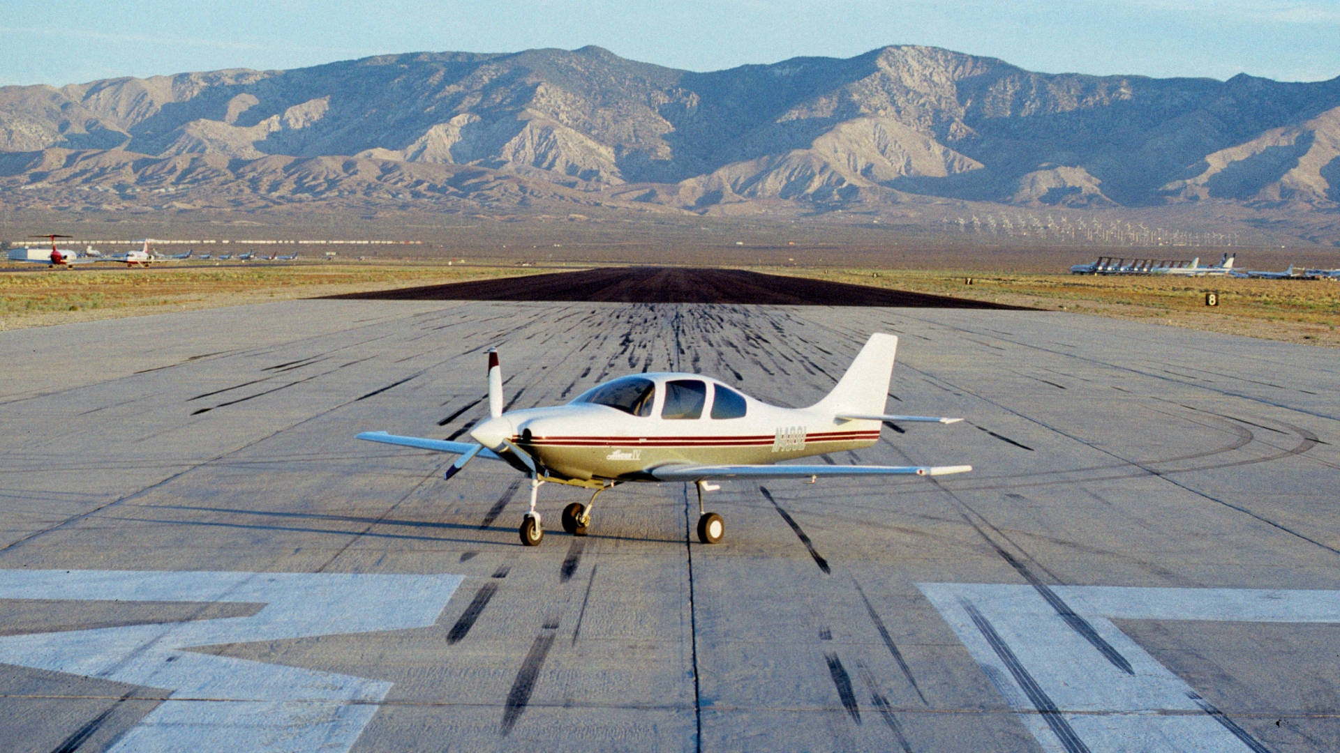 Runway 桌布 壁紙 — 一架白色小型螺旋槳飛機停在沙漠跑道上，背景是崎嶇的山脈，天空清澈湛藍。