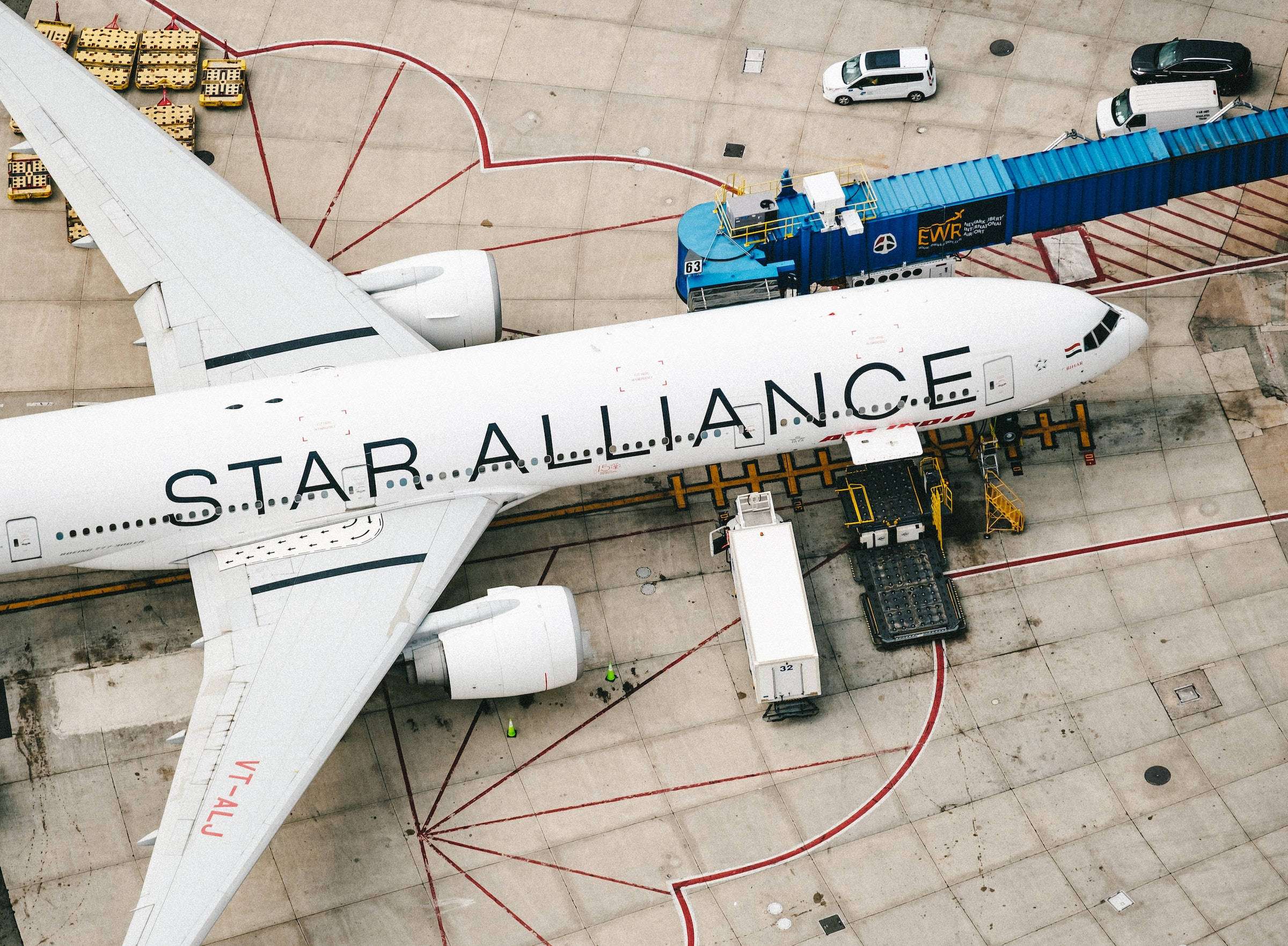 Airport 桌布 壁紙 — 一架白色星空聯盟飛機停泊在機場閘口，周圍有登機橋和地面車輛的鳥瞰圖。