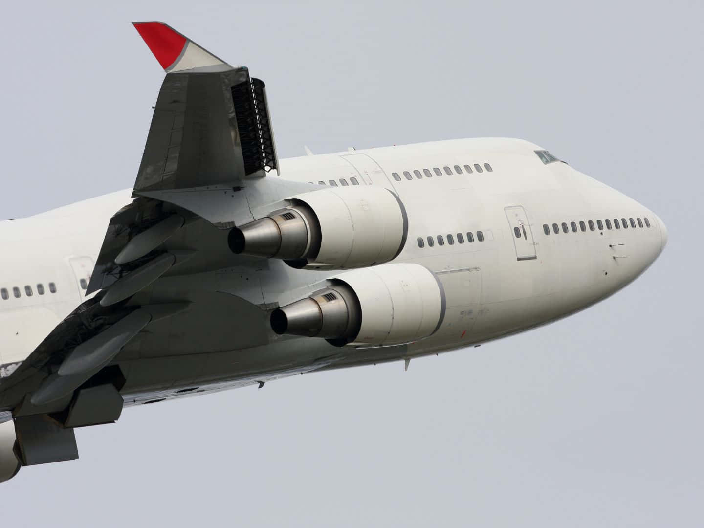 飛機 桌布 壁紙 — 一架白色波音747客機，紅色尾翼，在陰天翱翔，展示詳細的引擎和機身。