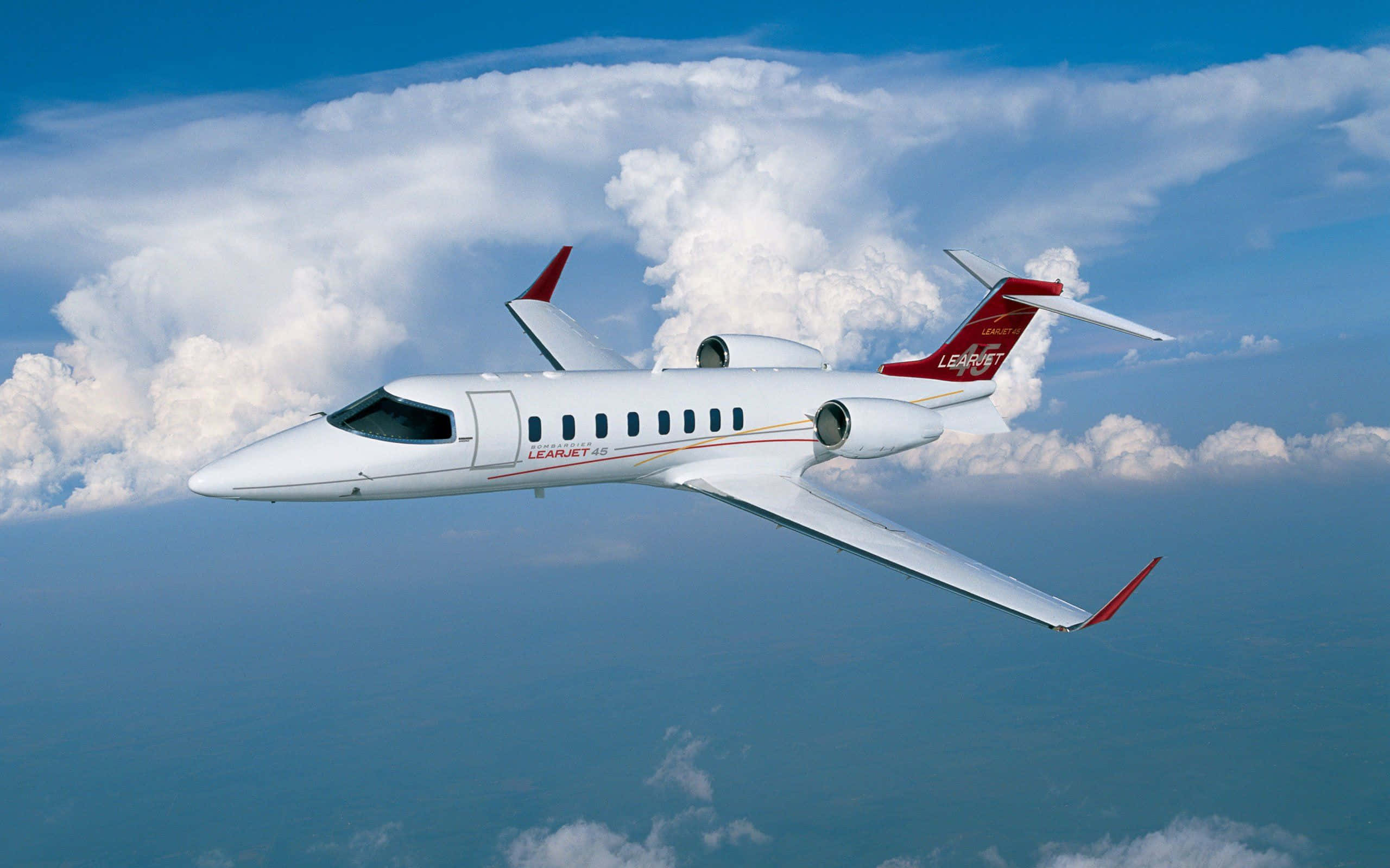 Jet 桌布 壁紙 — 一架白色的 Learjet 60 私人飛機在鮮藍色天空背景下，優雅地翱翔在蓬鬆的白色雲層之上。