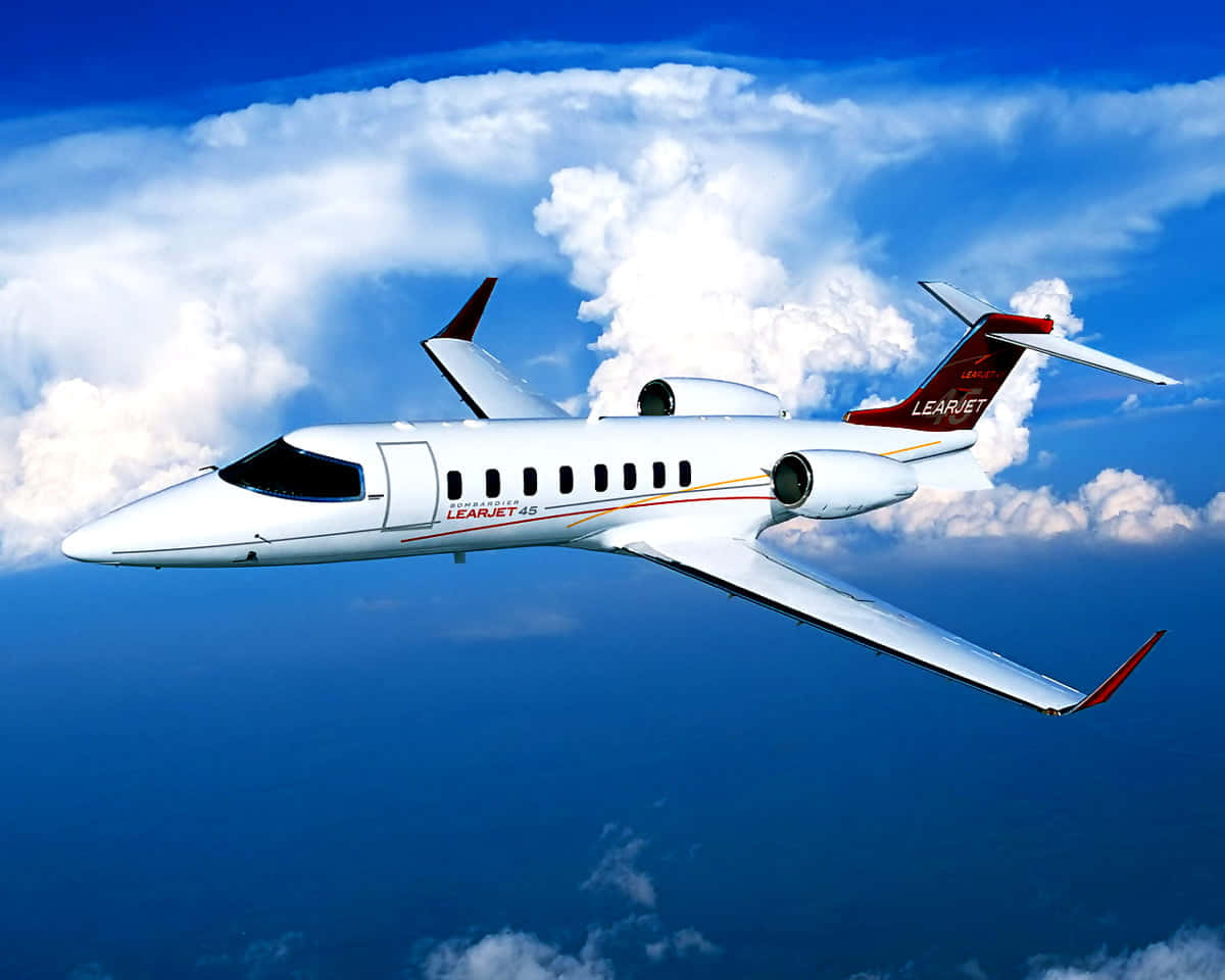 飛機 桌布 壁紙 — 一架白色的Learjet 45私人噴射機在鮮豔的藍天背景下優雅地翱翔在蓬鬆的白色雲層之上。