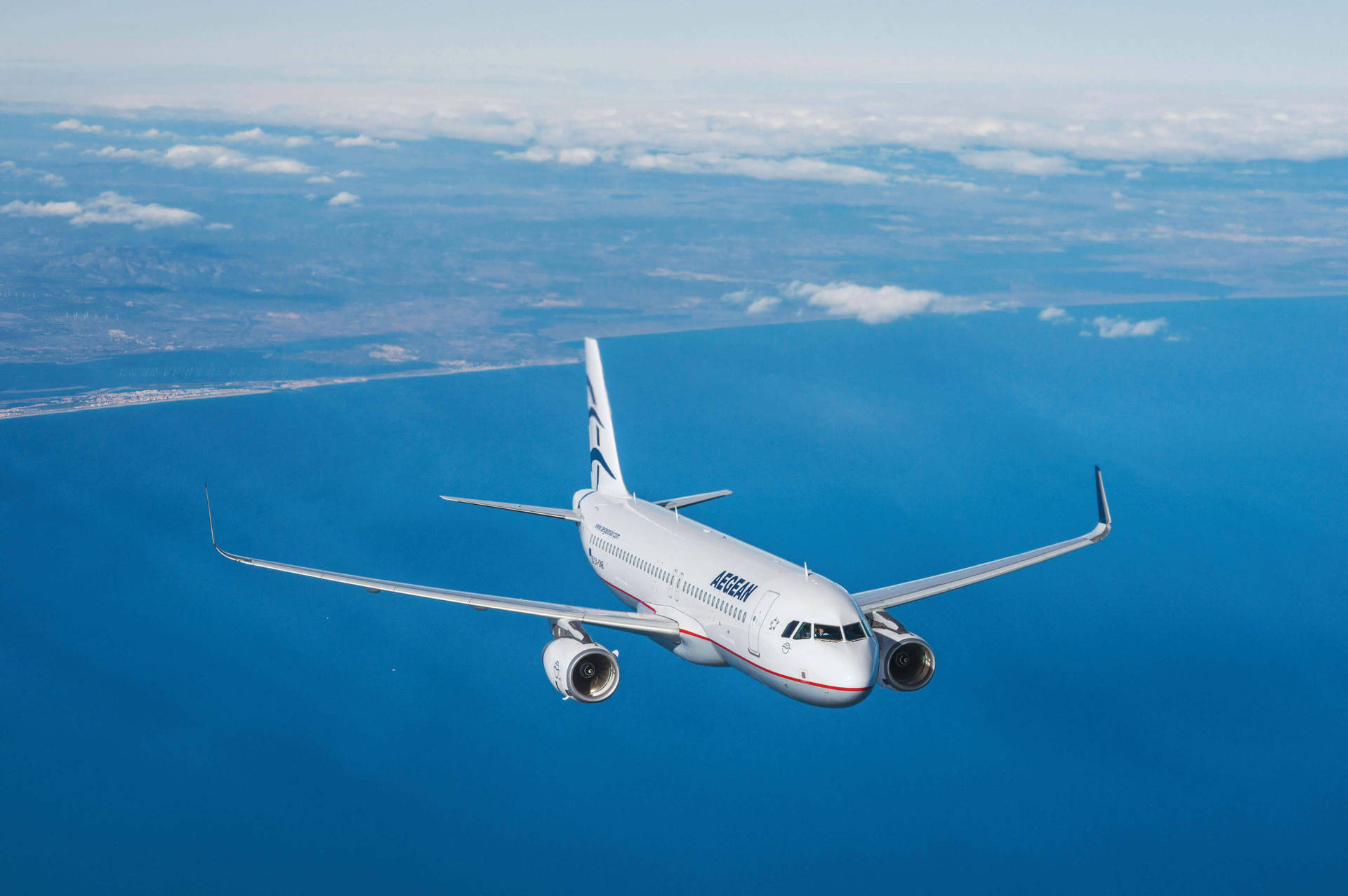  壁紙 — 一架白色的加拿大航空飛機在廣闊的藍色海洋上空翱翔，下方有散落的雲朵和遙遠的陸地。