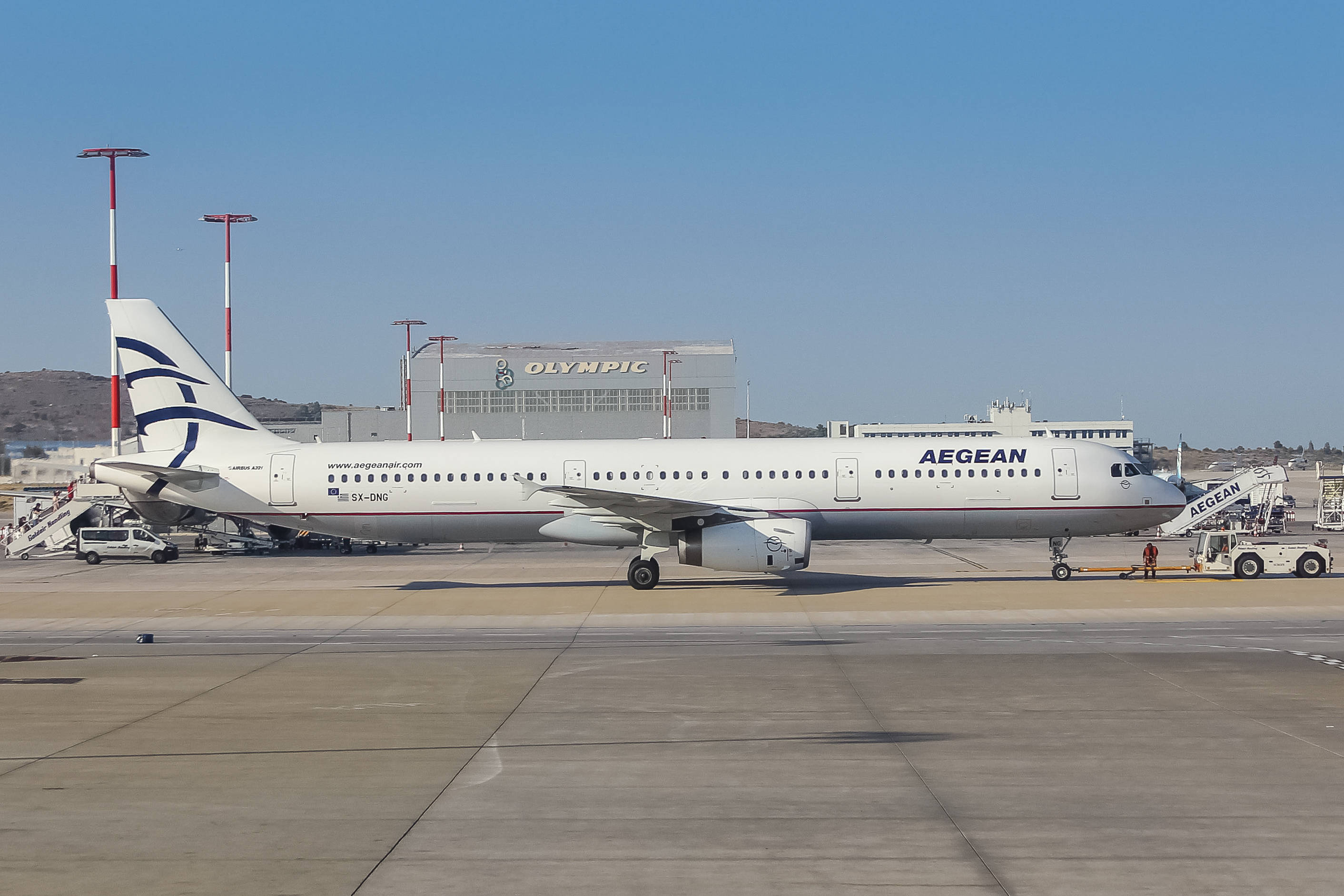 Airport 桌布 壁紙 — 一架白色的愛琴海航空空中巴士A320停在機場停機坪上，背景是晴朗的藍天和奧林匹克建築。