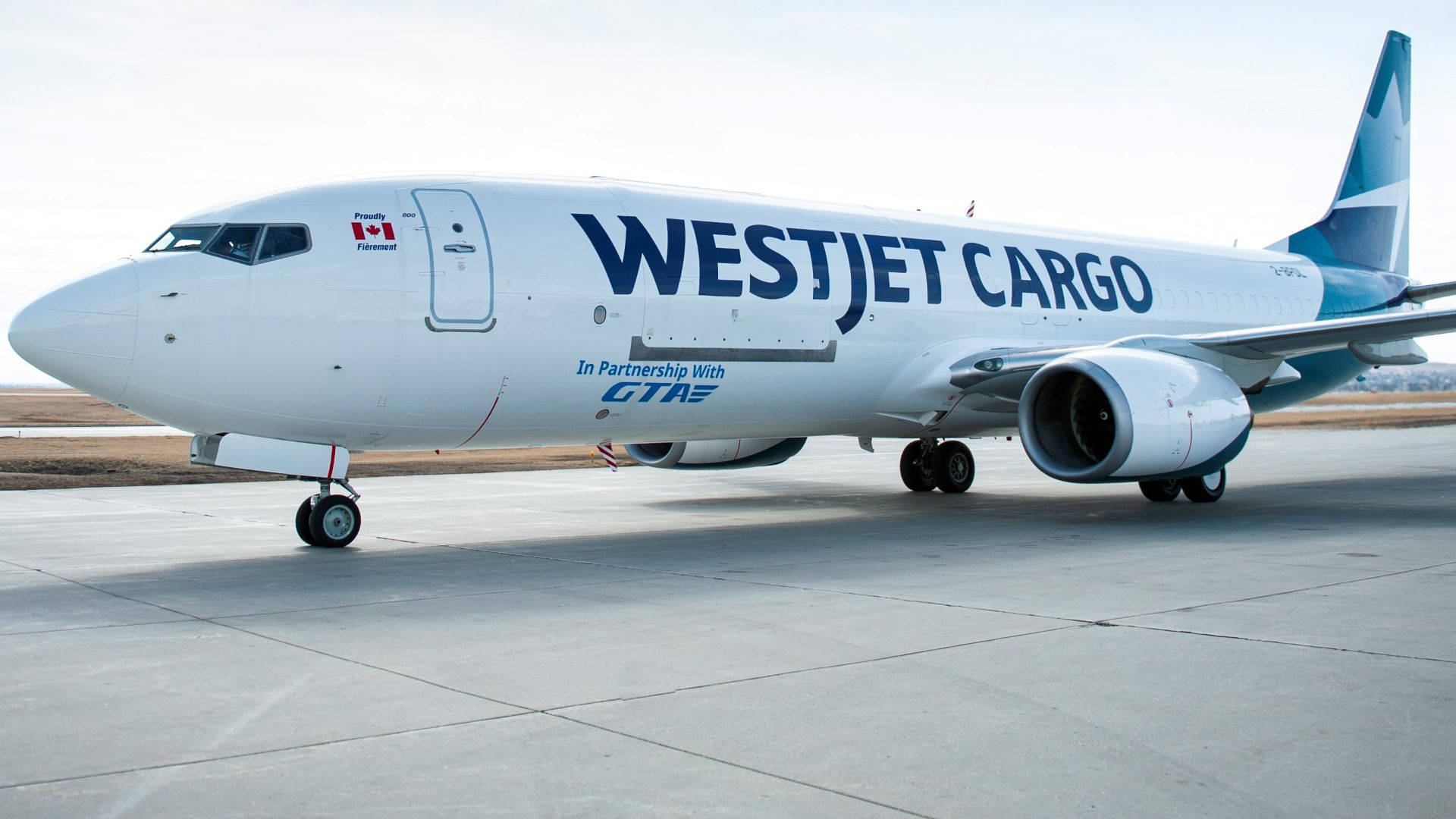 飛機 桌布 壁紙 — 一架白色的西捷航空貨運波音737停在停機坪上，天空多雲，起落架放下。