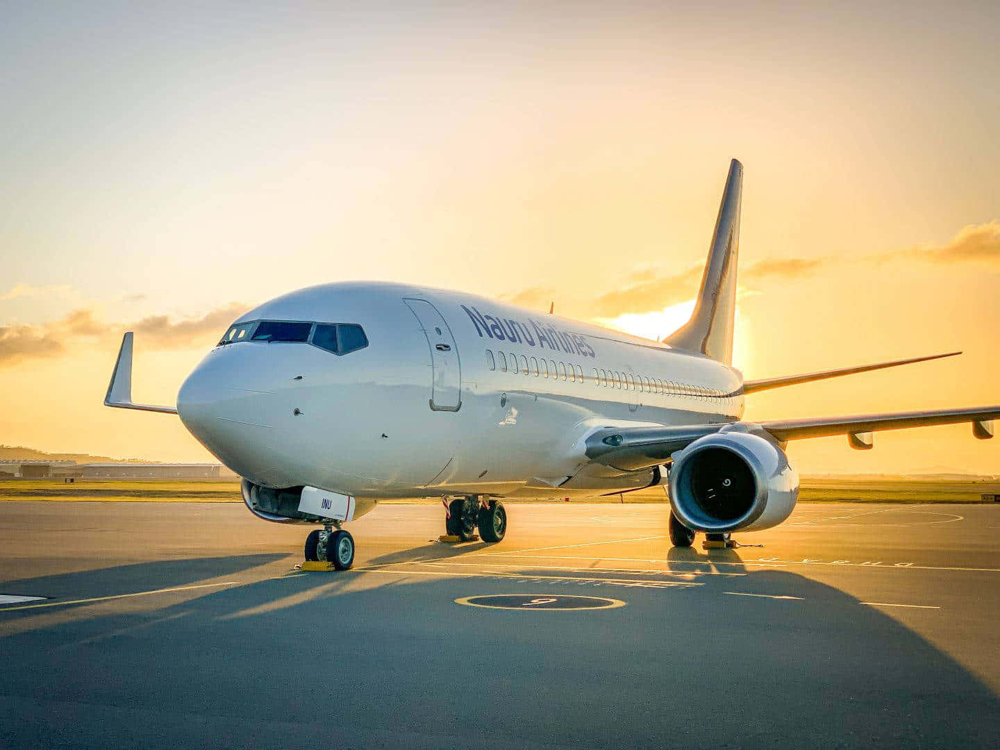 Runway 桌布 壁紙 — 一架白色的諾魯航空客機停在機場停機坪上，沐浴在金色的夕陽光中，投下長長的影子。