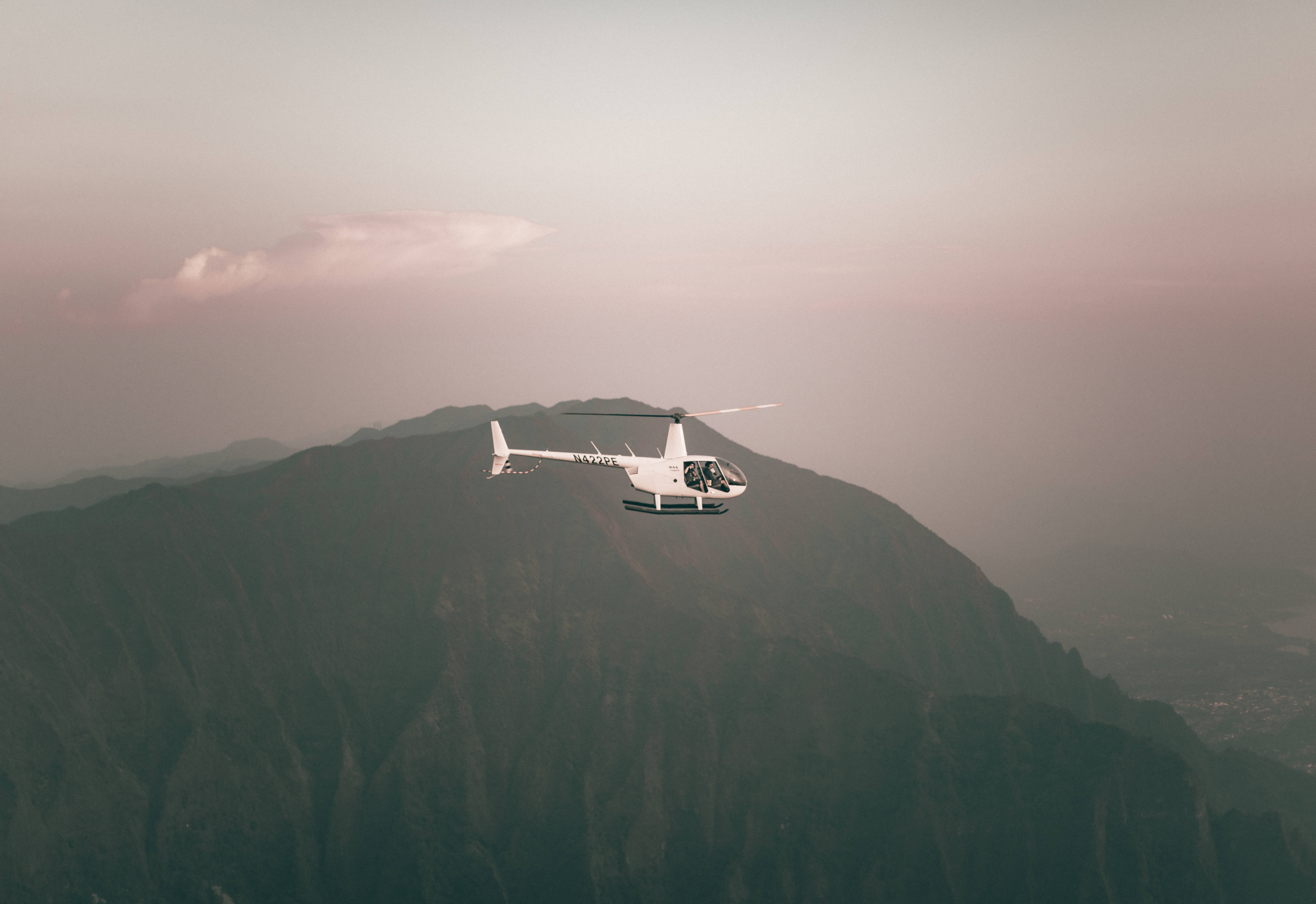 helicopter 4K 桌布 壁紙 — 一架白色直升機在柔和的粉紅色和灰色暮色天空下飛越崎嶇的山脈。