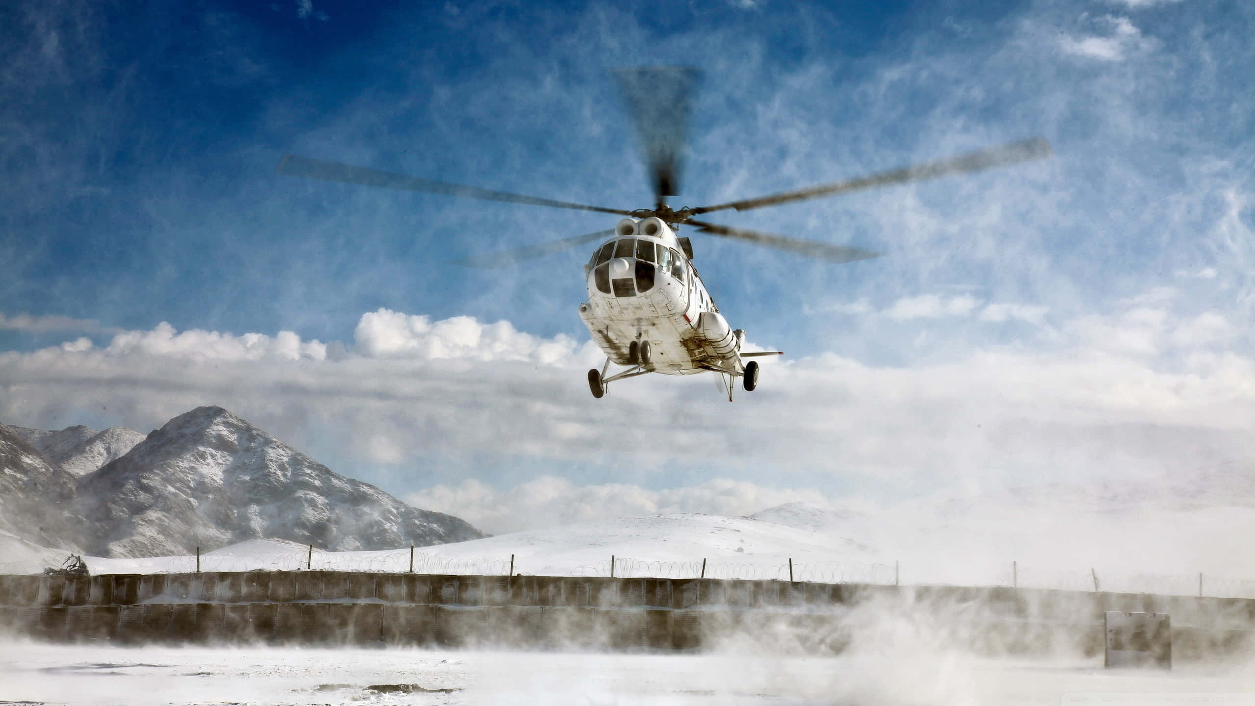 Helicopters 桌布 壁紙 — 一架白色直升機從積雪跑道起飛，揚起灰塵，背景是白雪覆蓋的山脈和明亮的藍天。