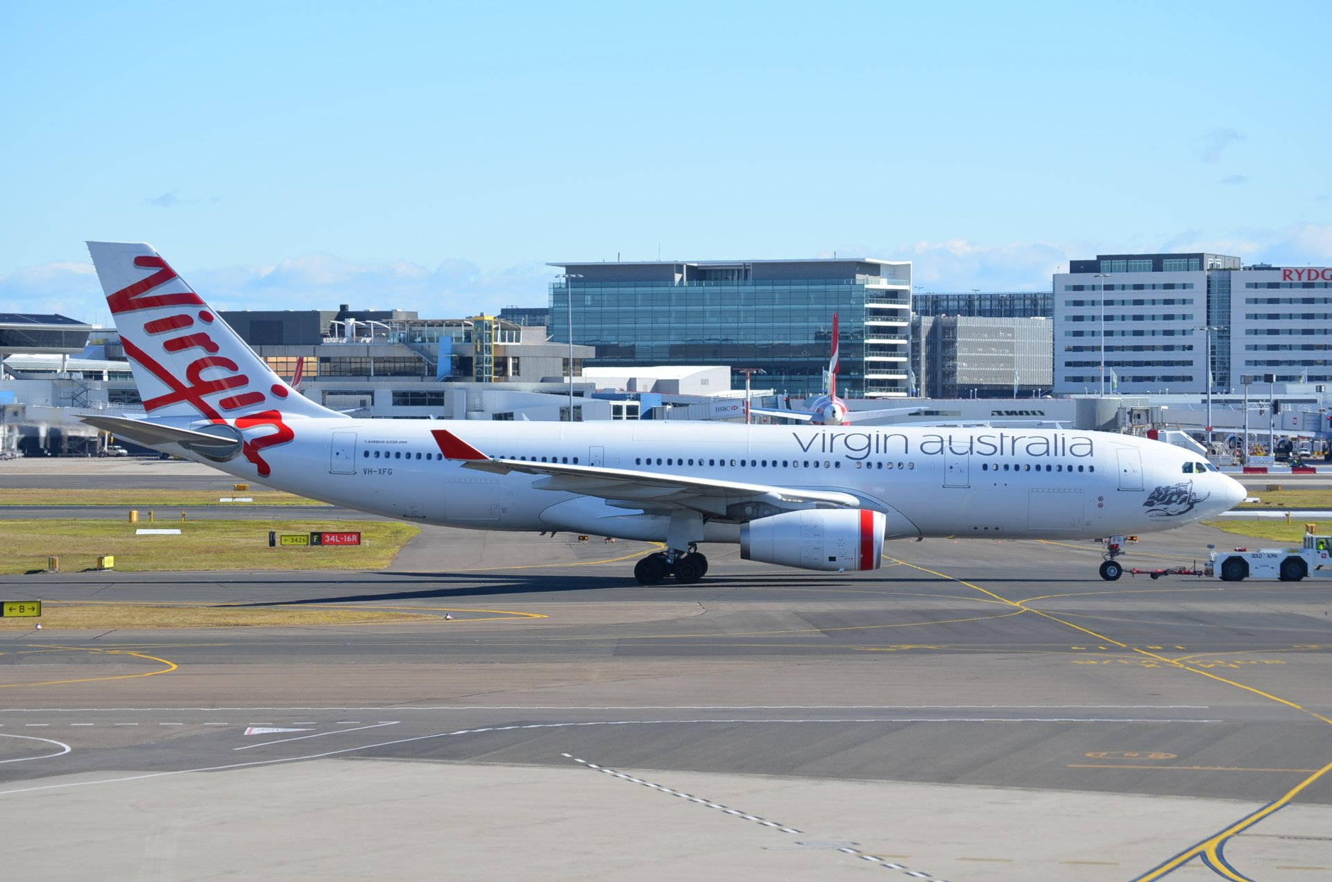  壁紙 — 一架白色維珍澳洲航空空中巴士A330在陽光明媚的機場停機坪上滑行，背景是現代化的航廈建築。