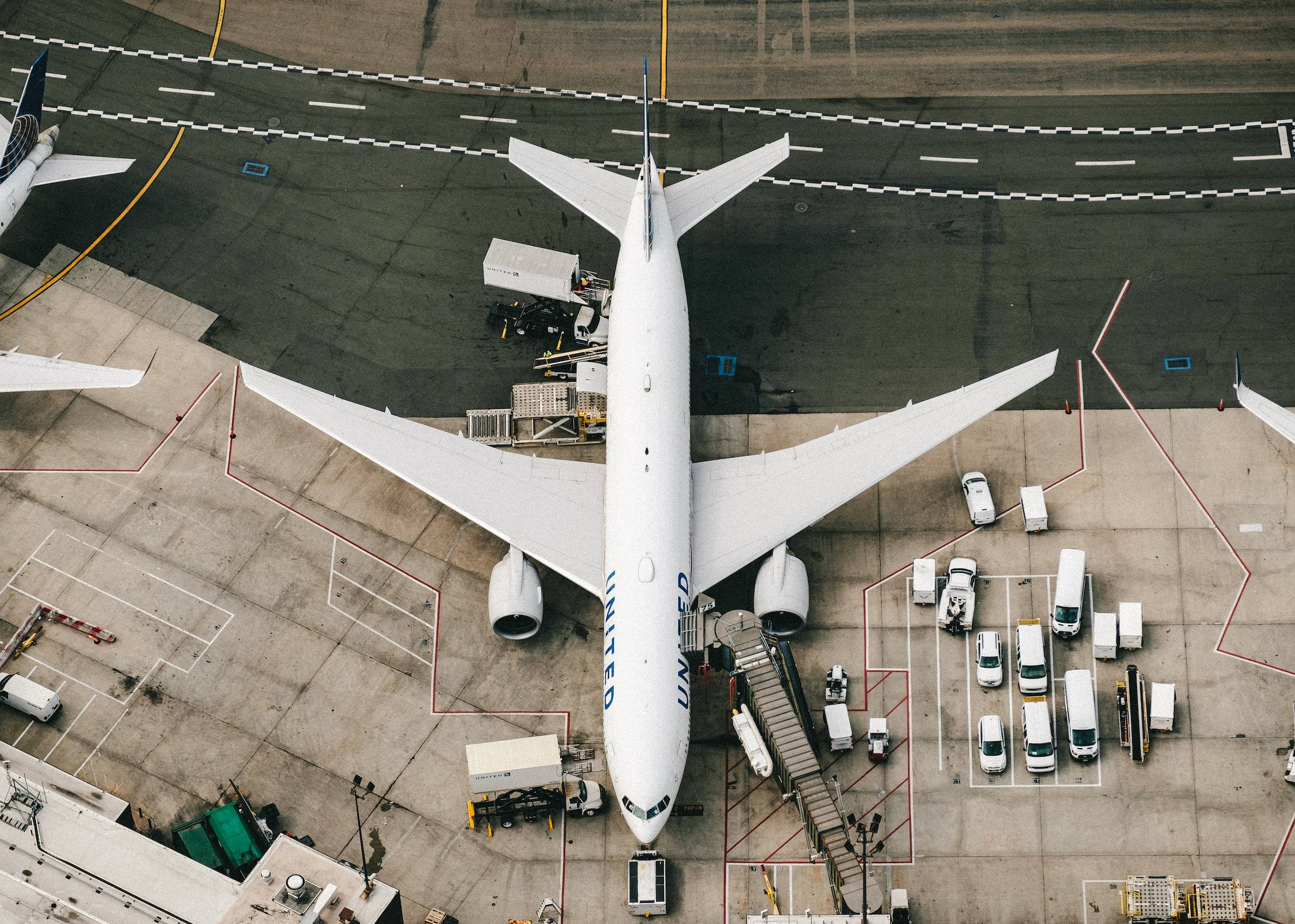 Airport 桌布 壁紙 — 一架白色聯合航空噴射機停泊在機場閘口，周圍有地勤服務車輛和設備的空中俯瞰圖。