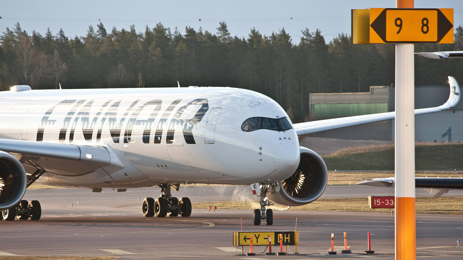 飛機 桌布 壁紙 — 一架白色芬蘭航空飛機在晴朗天空下，於機場停機坪上滑行，背景有跑道標誌和森林。
