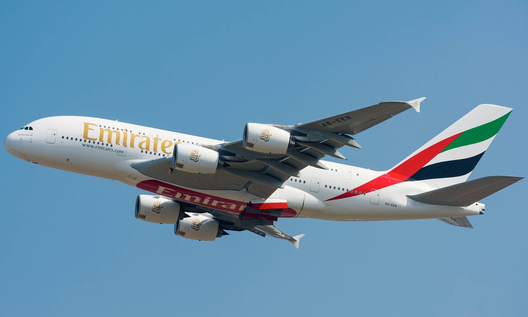 飛機 桌布 壁紙 — 一架白色阿聯酋航空空中巴士A380在清澈的藍天中翱翔，其標誌性的紅、綠、黑色尾翼清晰可見。