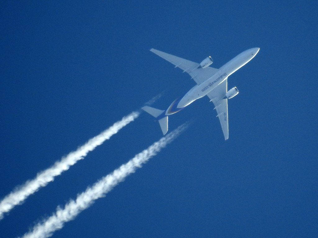 雲朵 桌布 壁紙 — 一架白色阿聯酋航空飛機在清澈的藍天中翱翔，留下兩道清晰的白煙。