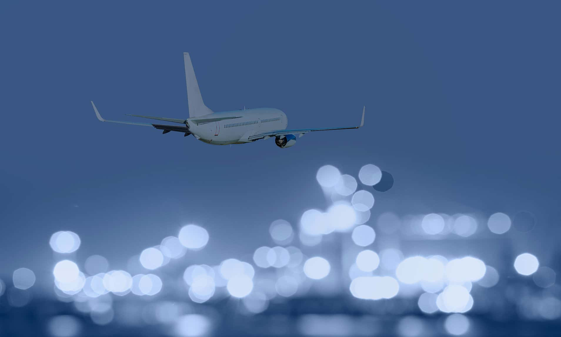 Aviation 桌布 壁紙 — 一架白色飛機在散景燈光照亮的機場航廈上空，於暮色天空中攀升。