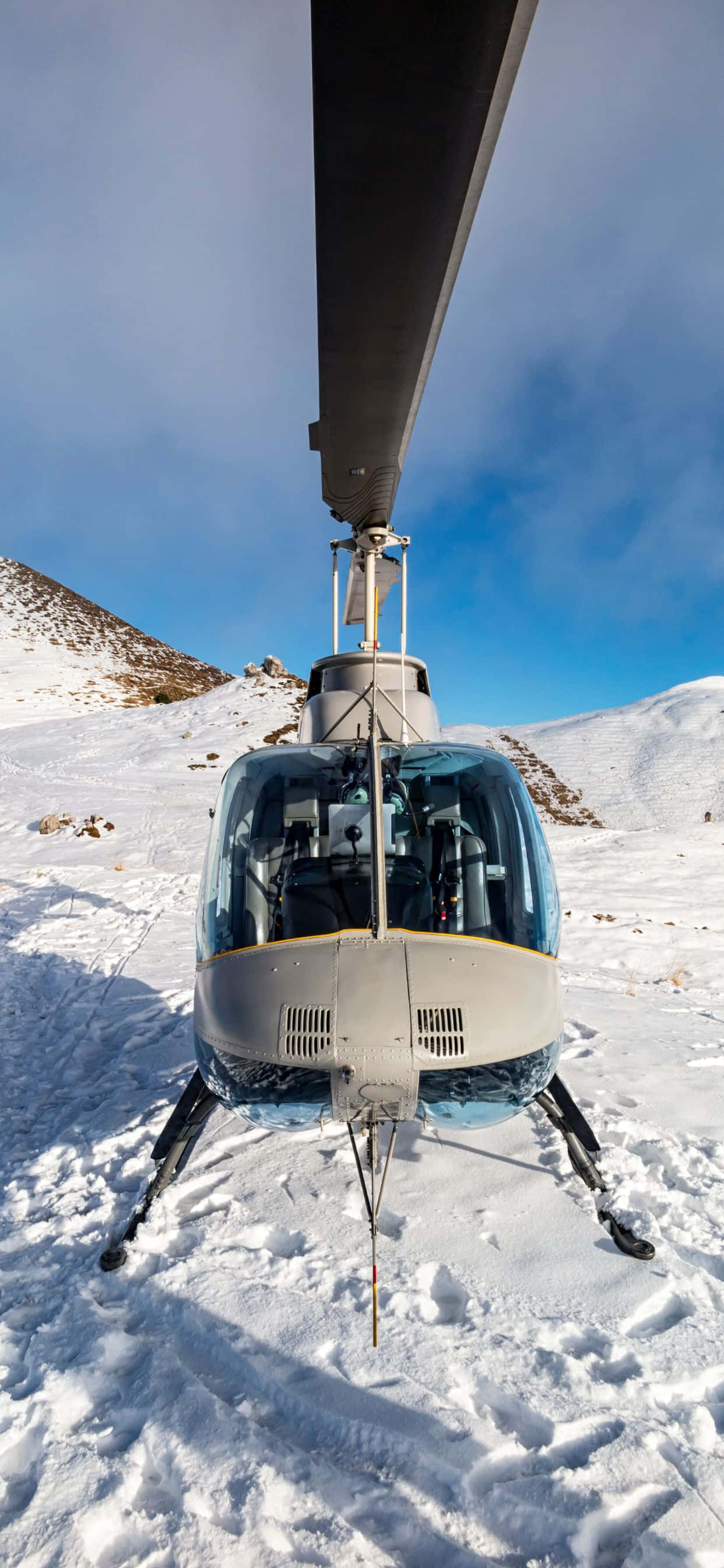 iPhone Xs Max Helicopters 桌布 壁紙 — 一架直升機停泊在白雪覆蓋的山坡上，背景是晴朗的藍天和崎嶇的山峰。