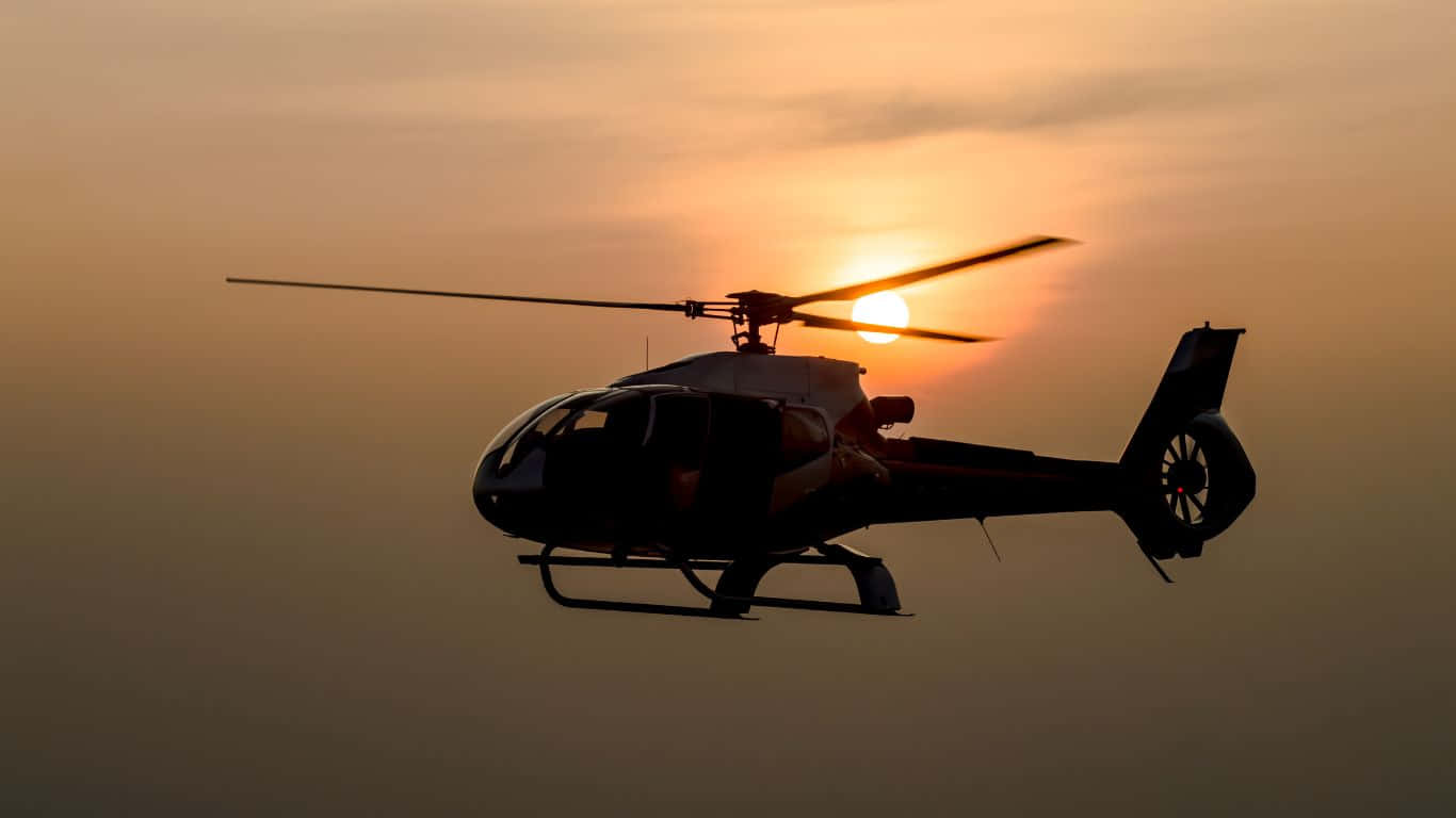 1366x768 Helicopters 桌布 壁紙 — 一架直升機在溫暖的橙色和粉紅色色調的發光日落天空襯托下的剪影。
