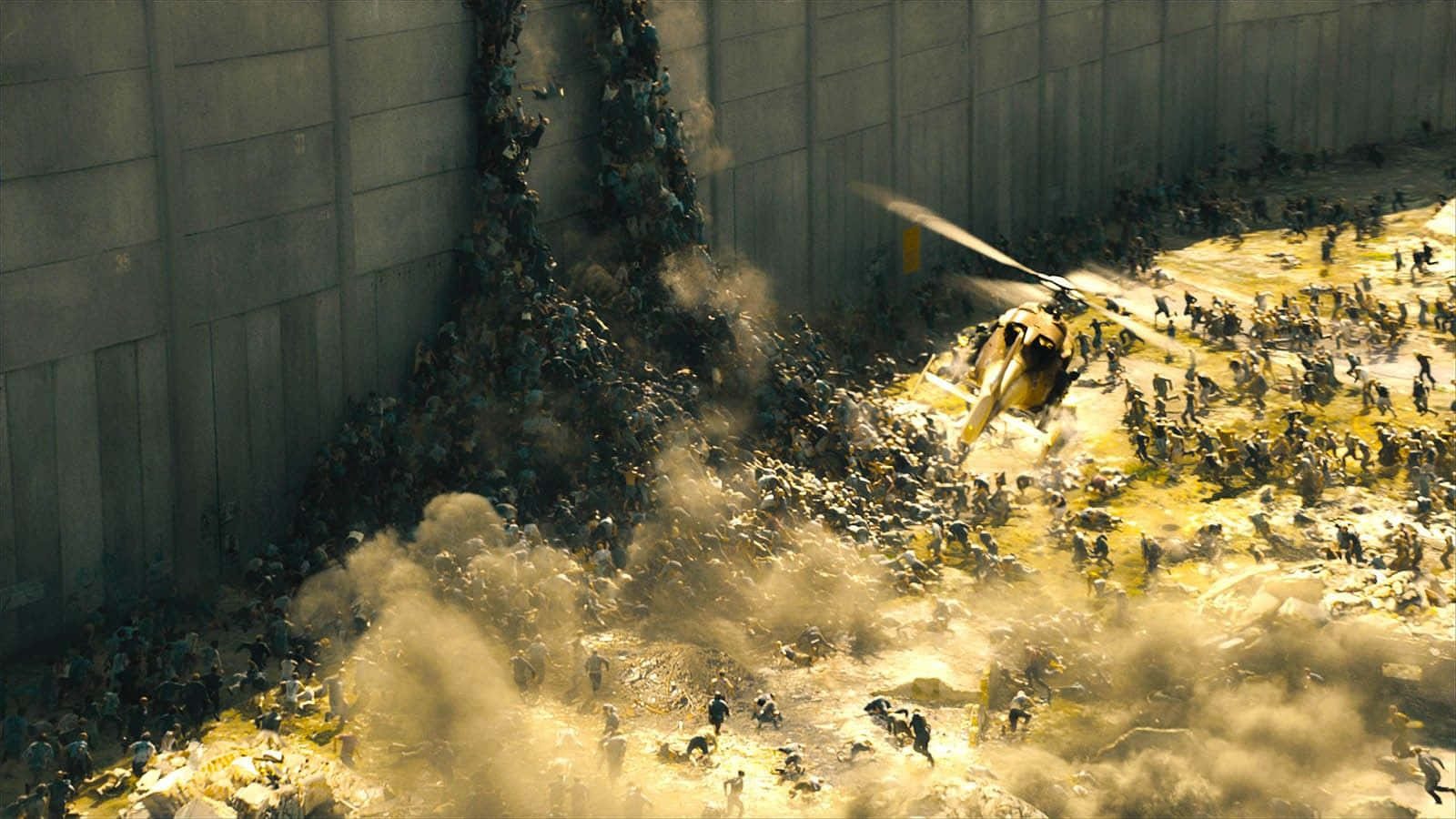 World War Z 桌布 壁紙 — 一架直升機盤旋在混亂的人群上方，人們正從倒塌的混凝土牆逃離，背景是塵土飛揚的城市廢墟。