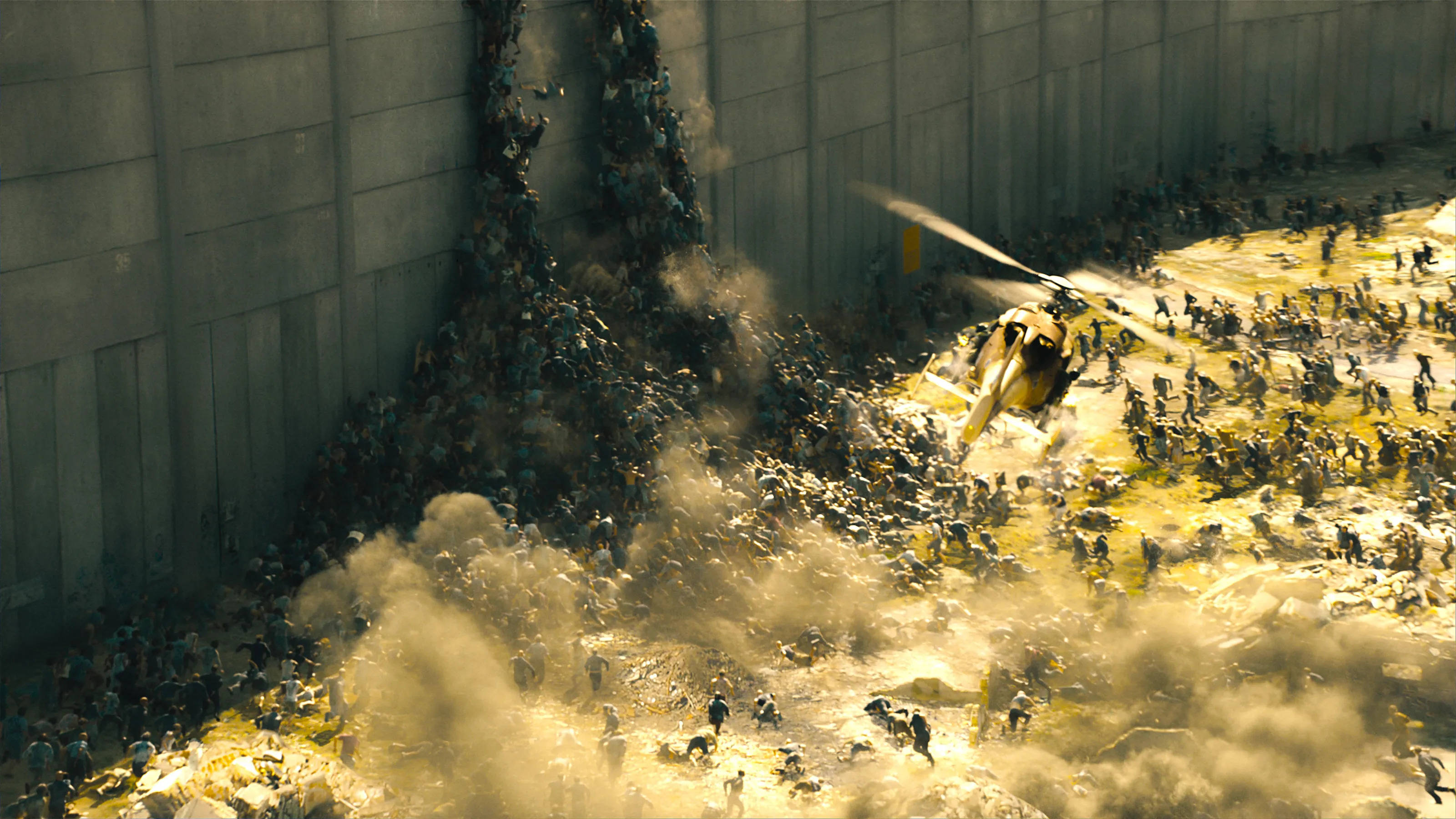 world war z 4K 桌布 壁紙 — 一架直升機盤旋在混亂的人群上方，人群正穿過高聳混凝土牆之間塵土飛揚的工業峽谷逃離。