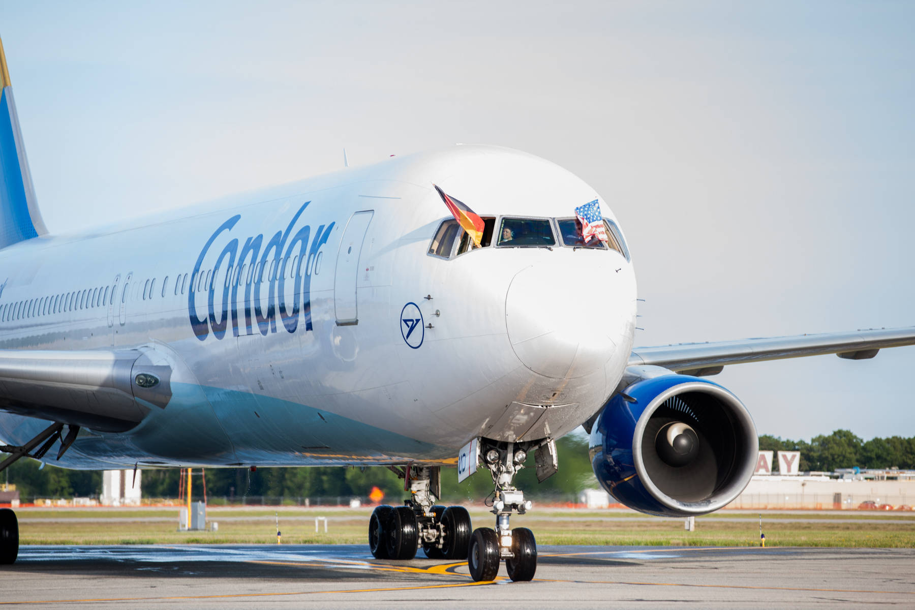飛機 桌布 壁紙 — 一架神鷹航空的噴射客機停在機場停機坪上，駕駛艙窗戶飄揚著德國和美國國旗，天空晴朗。