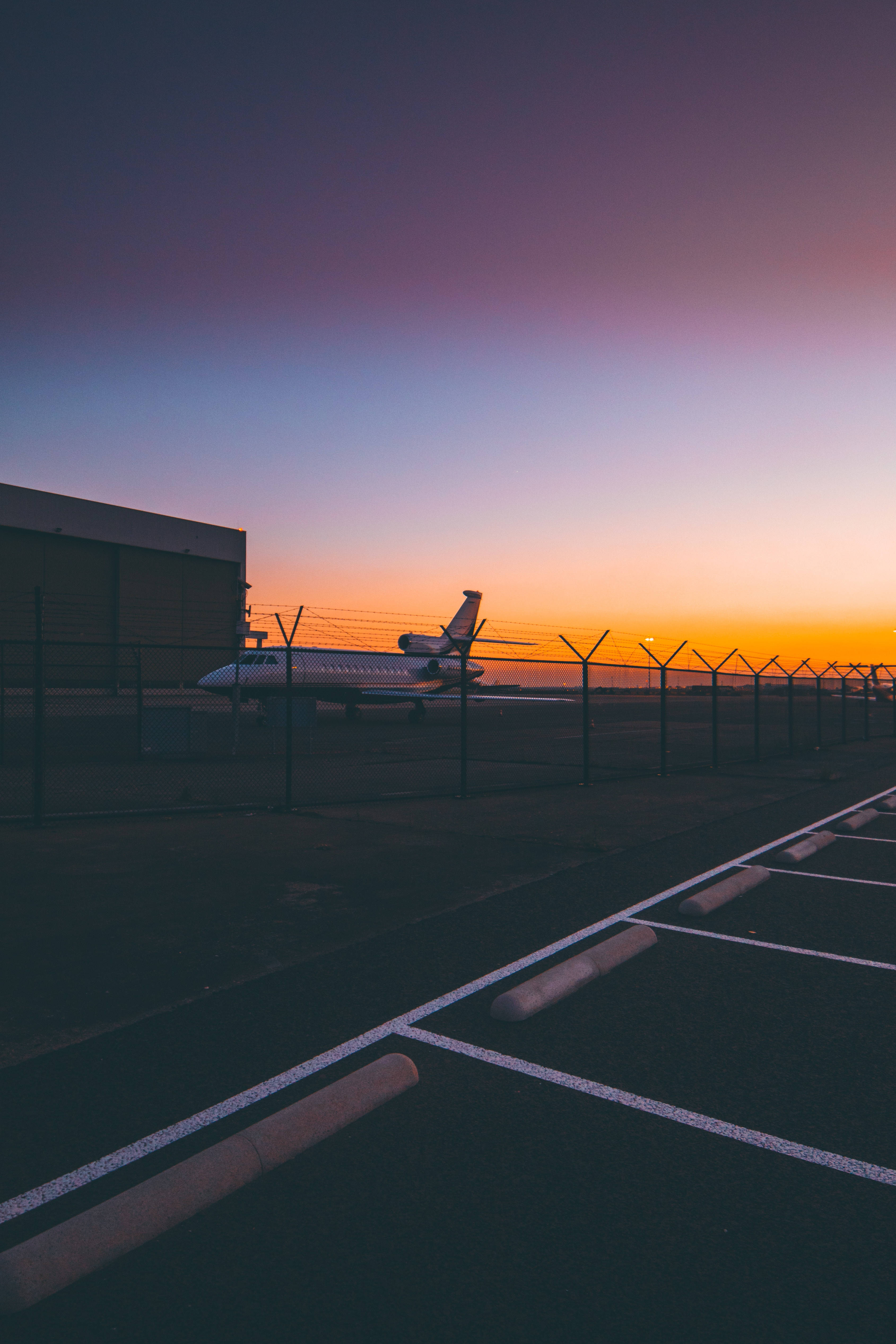 Airport 桌布 壁紙 — 一架私人飛機在黃昏時分停泊在圍欄後面，天空呈現紫、橙、藍的漸變色。