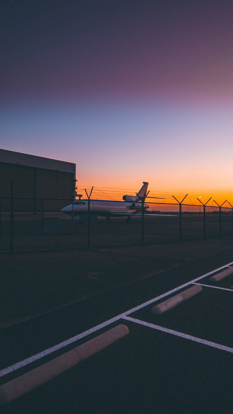 Airport 桌布 壁紙 — 一架私人飛機在黃昏時分停泊在圍欄後面，天空呈現紫色、橙色和藍色的漸變色。