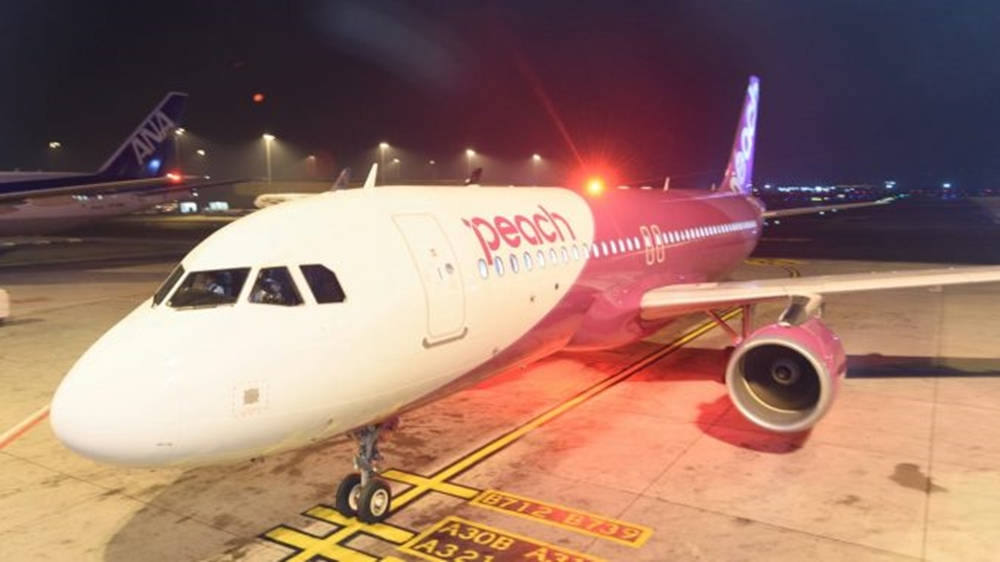 Plane 桌布 壁紙 — 一架粉紅色和白色的Peach Airlines飛機在夜間停泊在燈光明亮的機場停機坪上，地面有黃色標記。