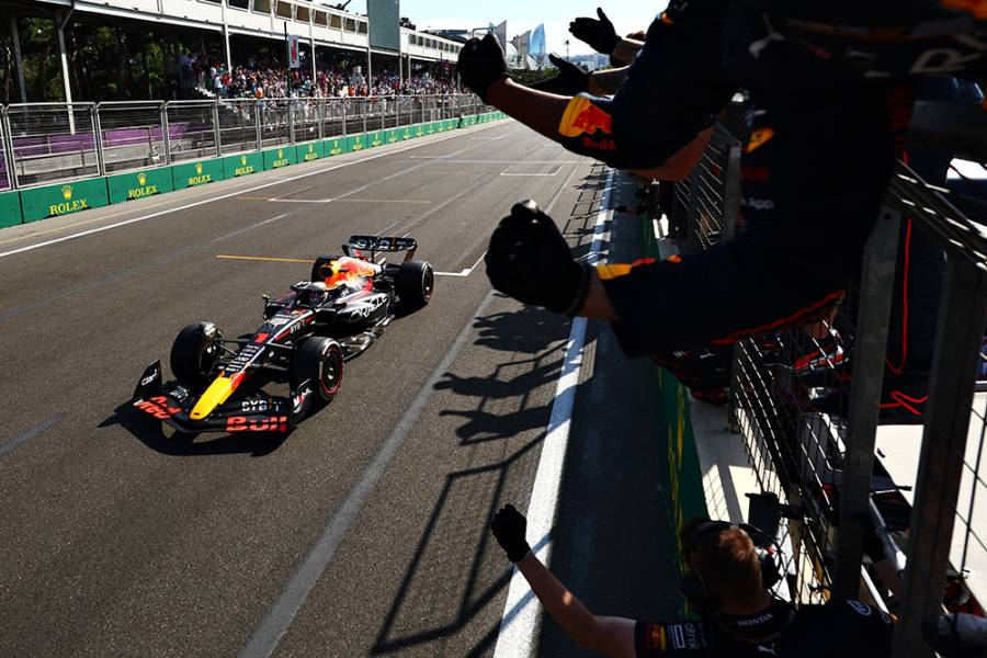Red Bull 桌布 壁紙 — 一架紅牛一級方程式賽車在陽光明媚的賽道上飛馳而過，旁邊是歡呼的車隊成員。