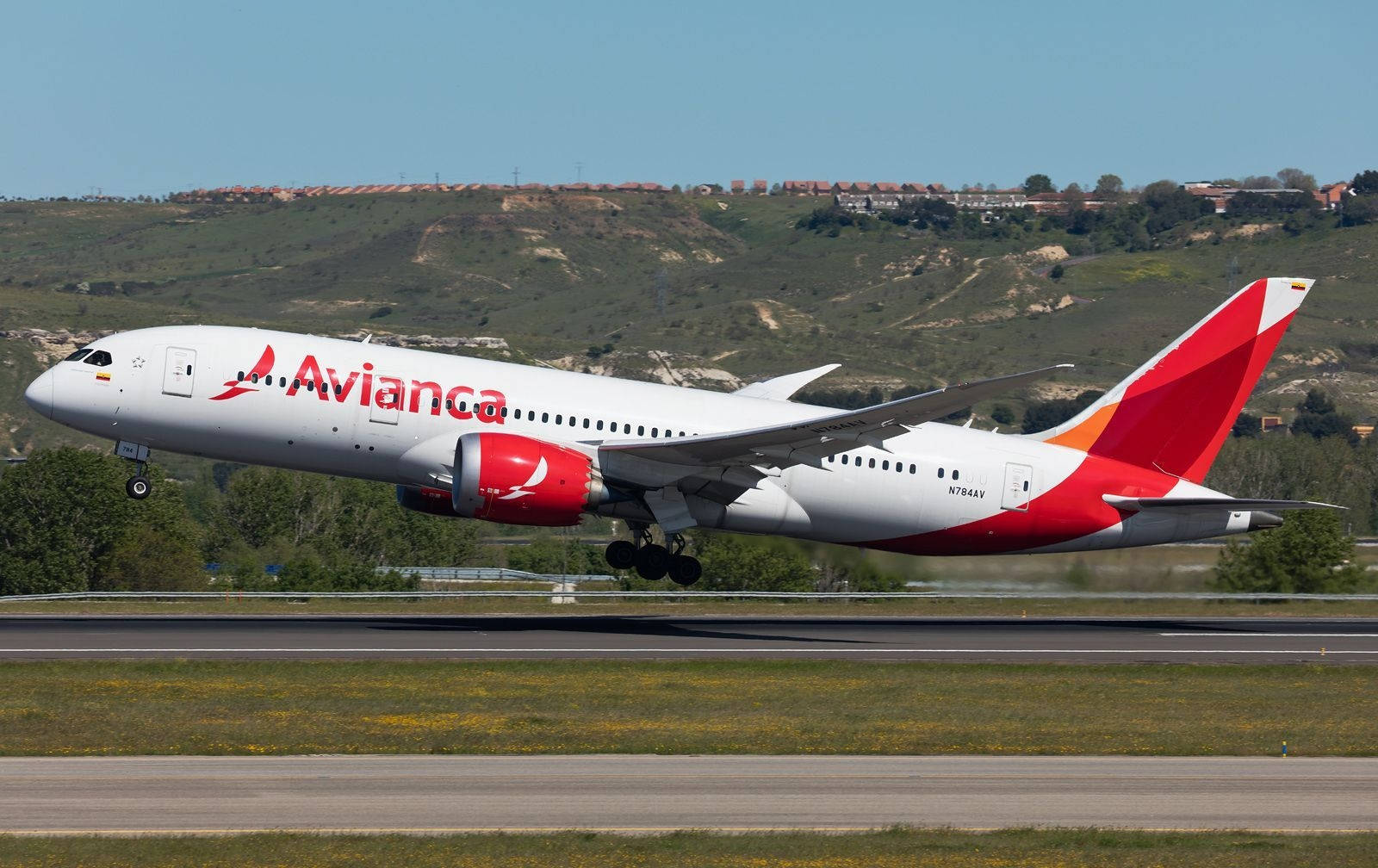Plane 桌布 壁紙 — 一架紅白塗裝的 Avianca 客機在綠色山丘和晴朗藍天的背景下從跑道起飛。