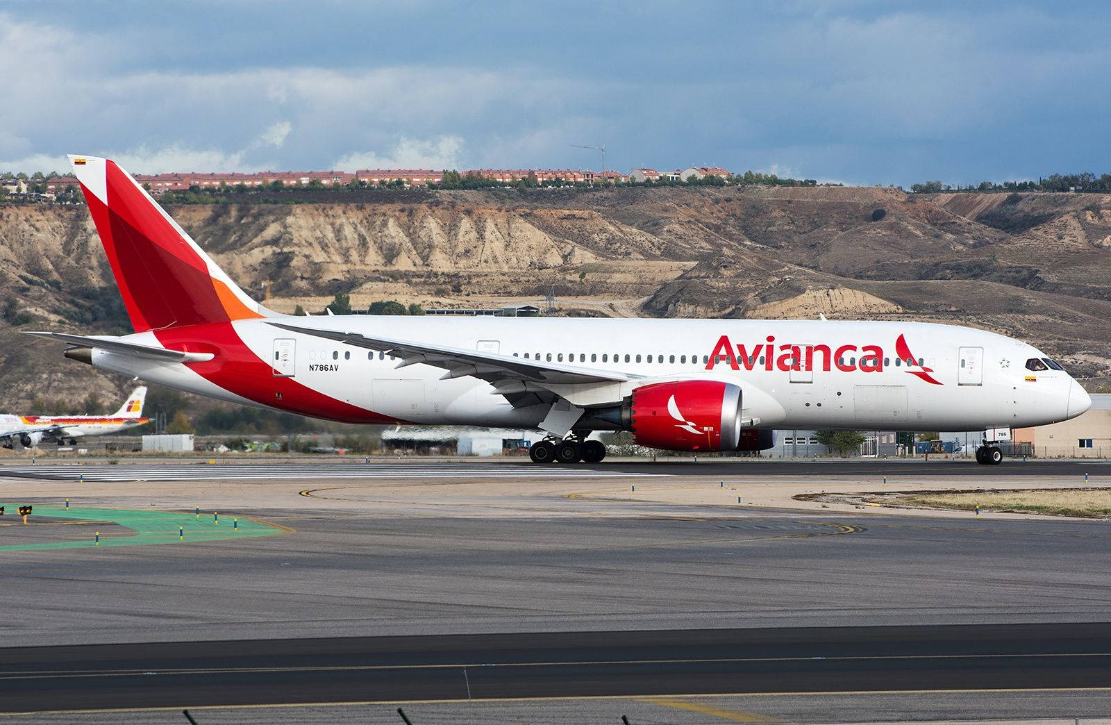 Plane 桌布 壁紙 — 一架紅白塗裝的Avianca客機在跑道滑行，背景是乾燥的山丘和多雲的天空。