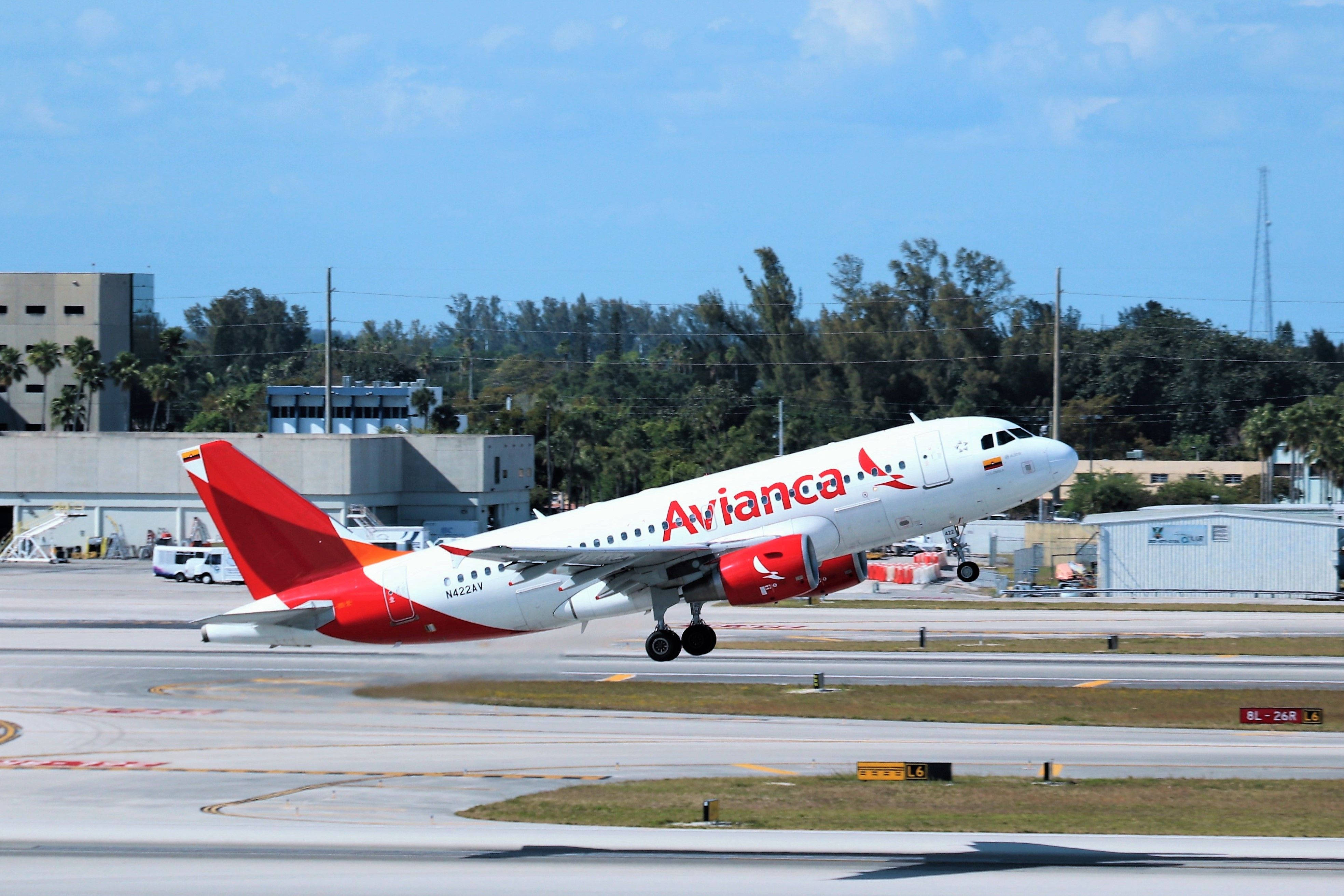 Plane 桌布 壁紙 — 一架紅白塗裝的Avianca飛機在陽光普照的機場跑道上起飛，背景有棕櫚樹和機庫。