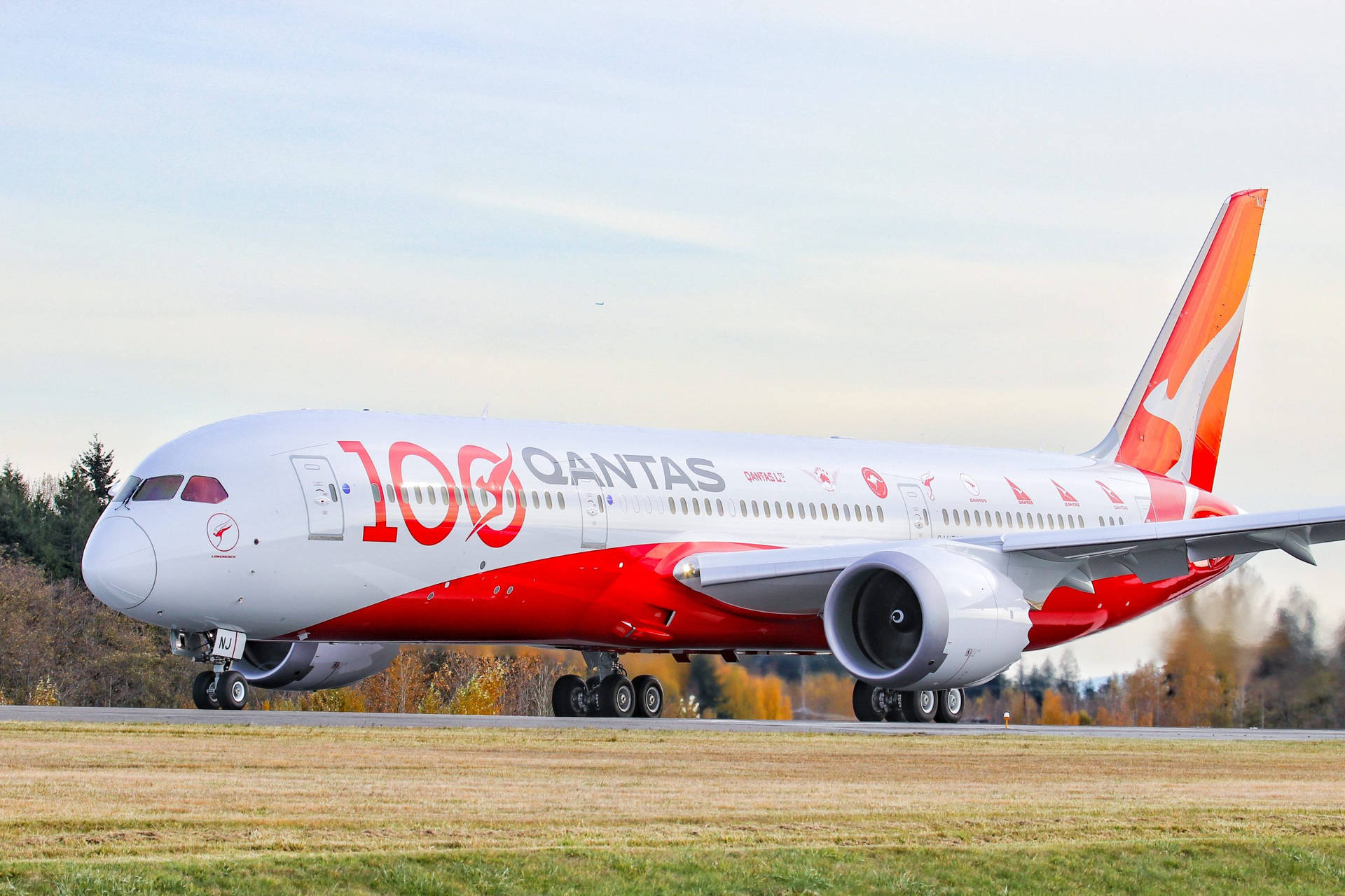 Airport 桌布 壁紙 — 一架紅白塗裝的澳洲航空787夢幻客機在淡色天空下，於被秋樹環繞的跑道上滑行。