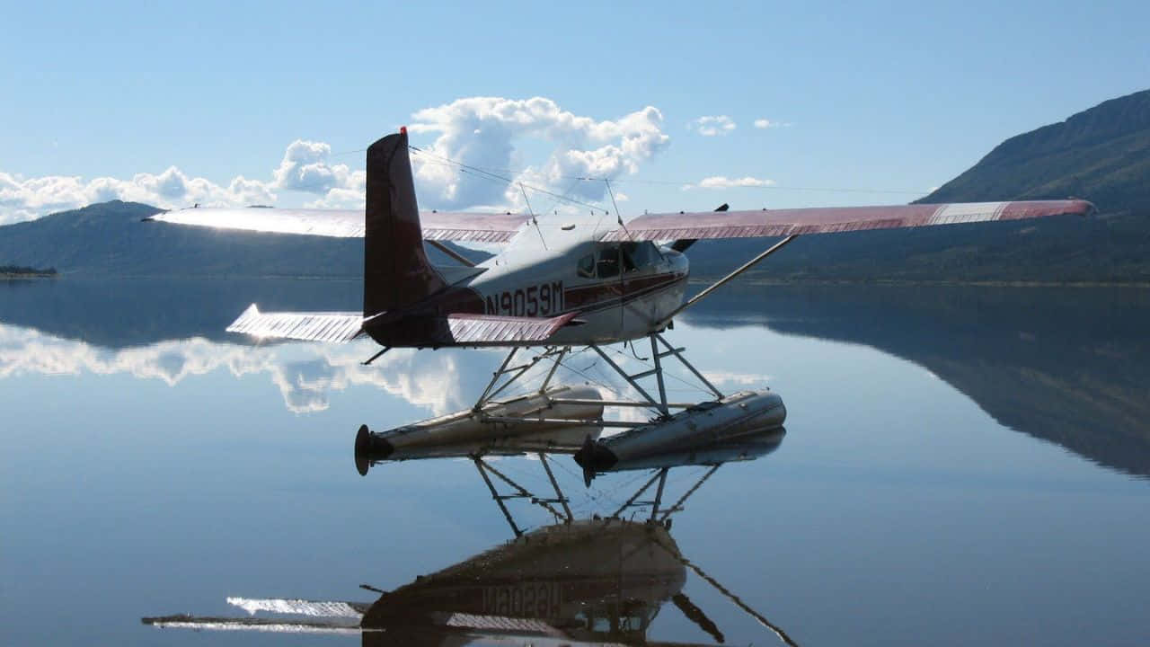 720p Plane 桌布 壁紙 — 一架紅白條紋的水上飛機在清澈藍天下，靜靜漂浮在如鏡的湖面上，倒映著山巒和白雲。