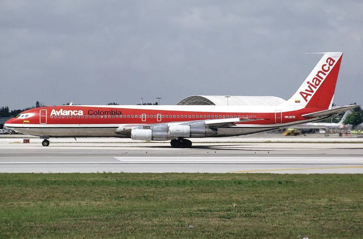  壁紙 — 一架紅白相間的 Avianca Colombia 波音 767 停放在機場停機坪上，天空多雲，前景有草地。