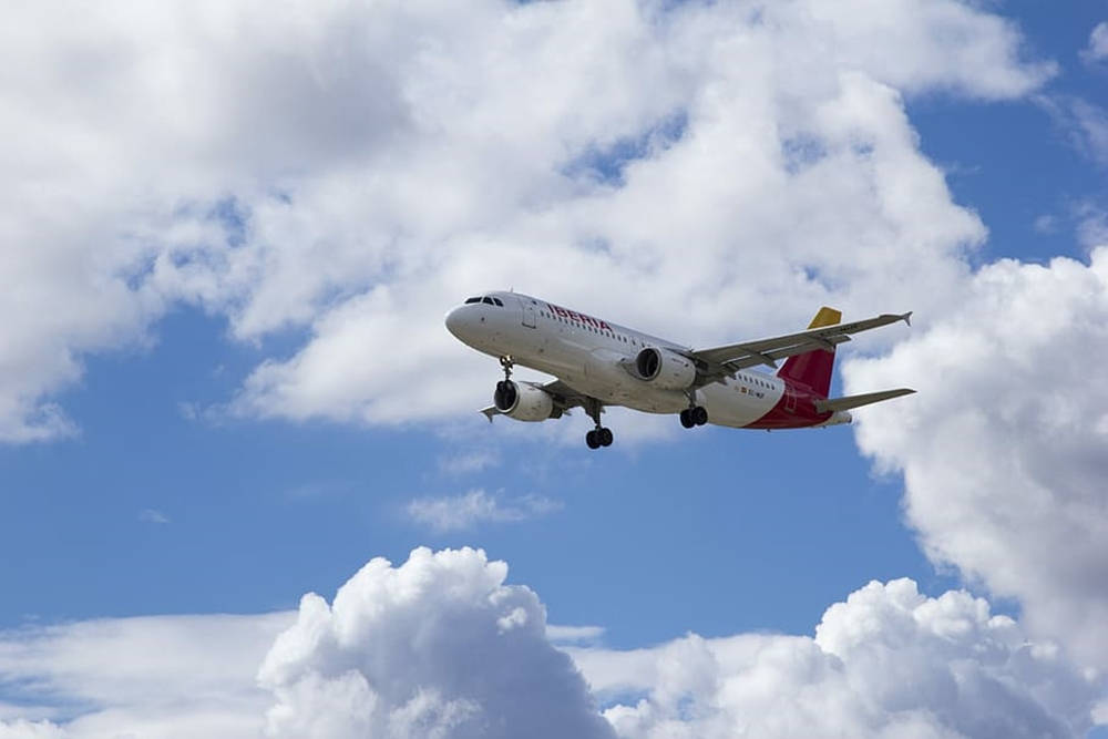 flying 桌布 壁紙 — 一架紅白相間的飛機放下起落架，在佈滿蓬鬆白雲的明亮藍天中翱翔。