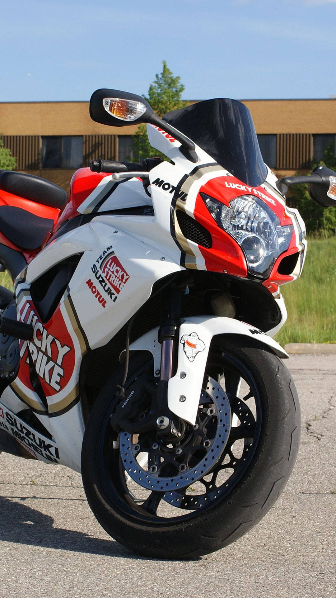  壁紙 — 一架紅白色Suzuki機車帶有Lucky Strike品牌標誌，停泊在柏油路上，天空清澈湛藍。
