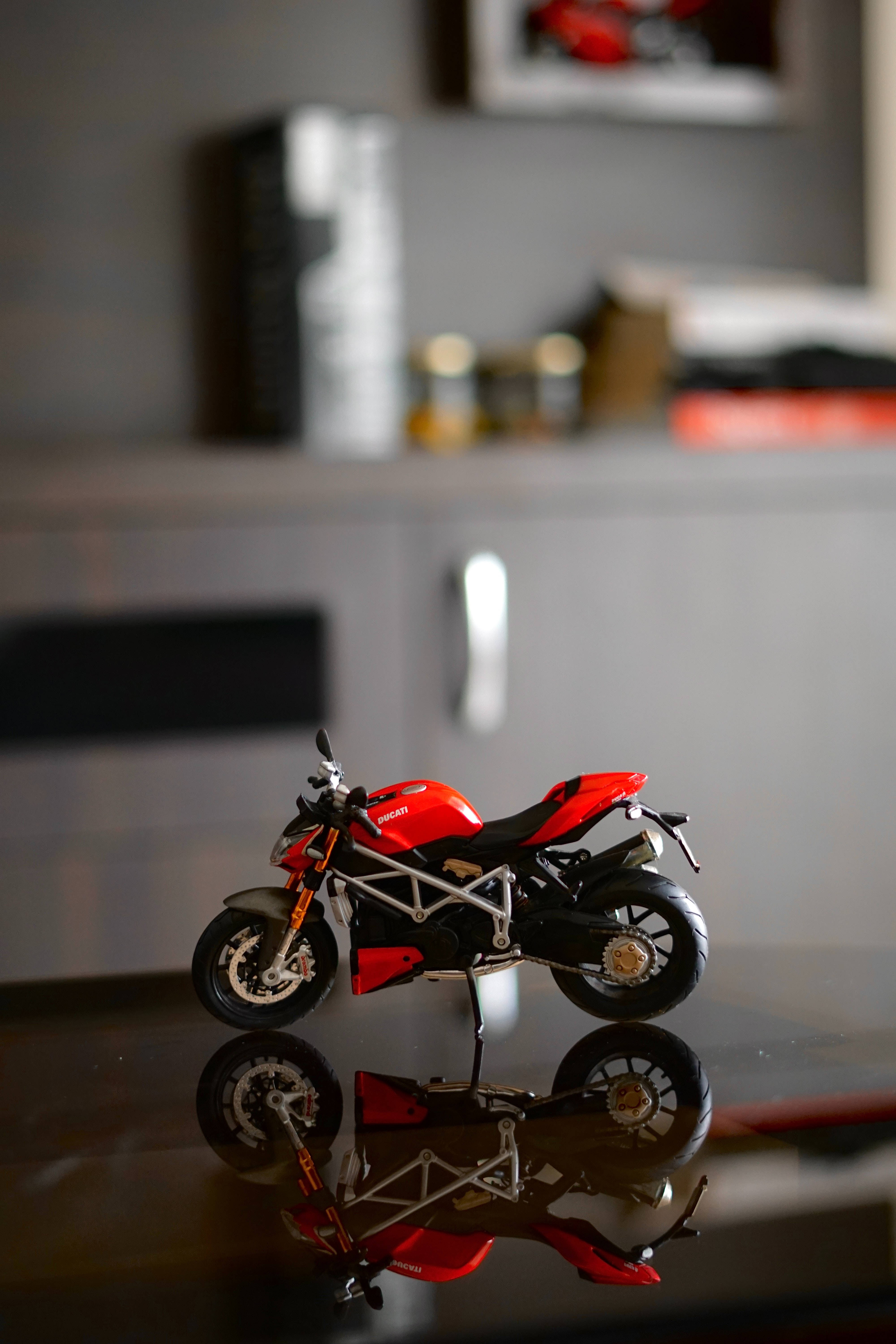 機車 桌布 壁紙 — 一架紅色Ducati機車模型放在光滑的黑色表面上，帶有清晰的倒影和模糊的灰色機艙背景。