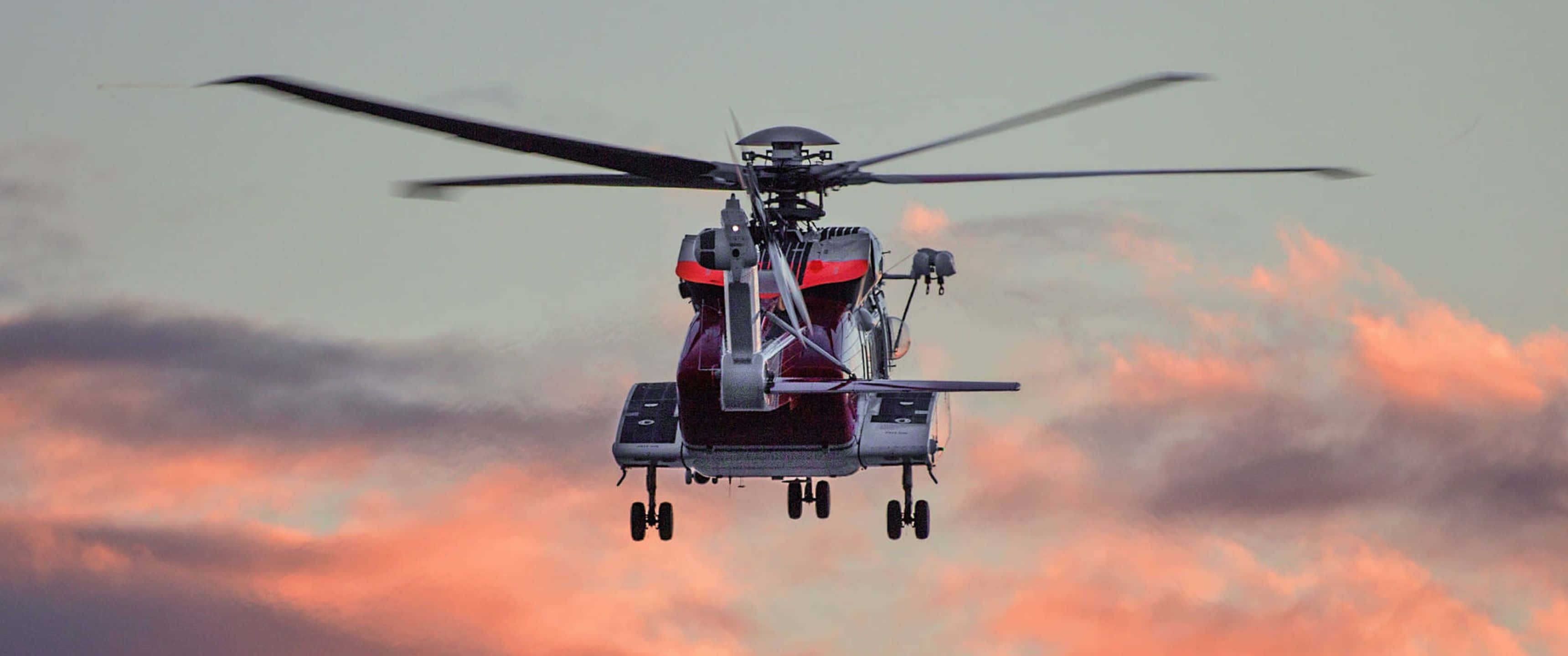 3440x1440p Helicopters 桌布 壁紙 — 一架紅色和灰色的直升機在橙紫色雲彩的戲劇性日落天空背景下飛行。