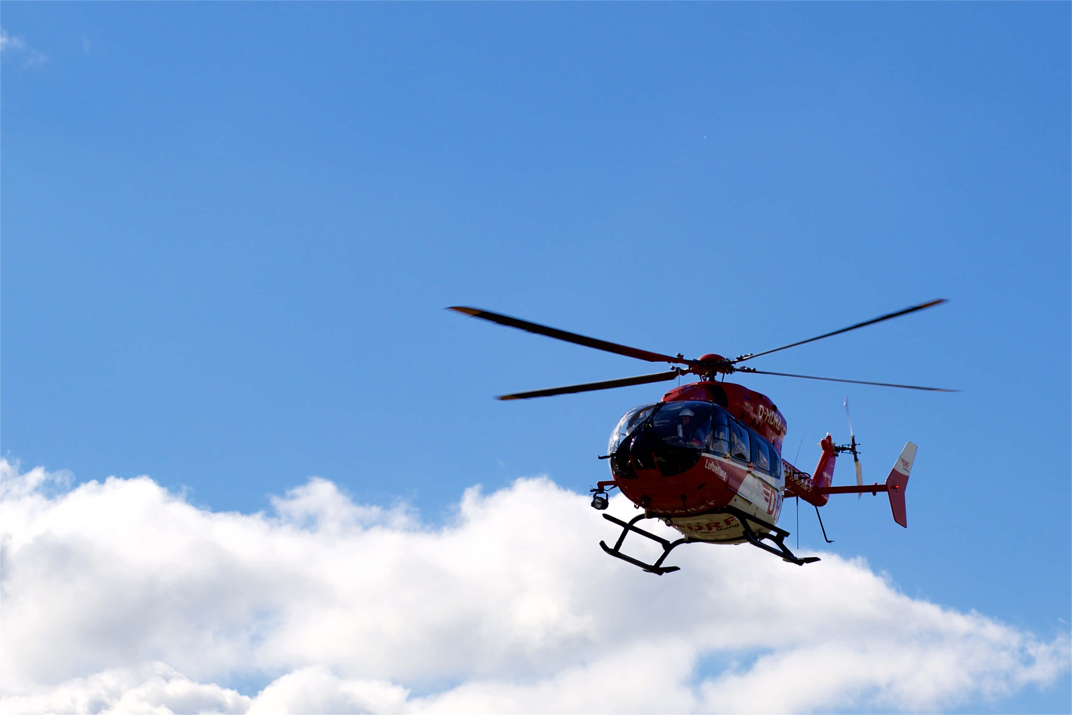 Helicopter 桌布 壁紙 — 一架紅色救援直升機在明亮的藍天中翱翔，下方有蓬鬆的白雲。
