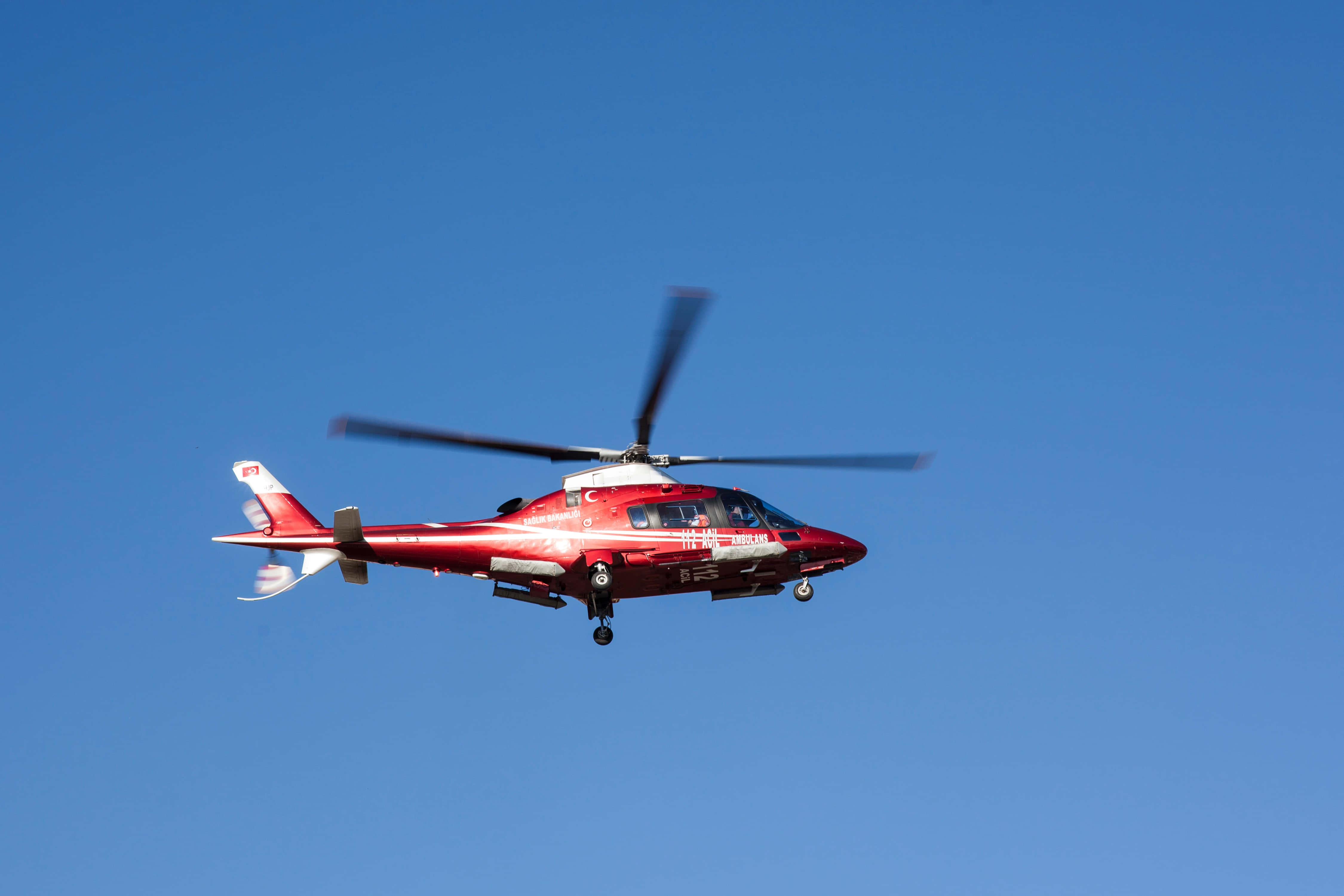 Helicopter 桌布 壁紙 — 一架紅色救援直升機在晴朗的藍天中翱翔，旋翼轉動，起落架放下。