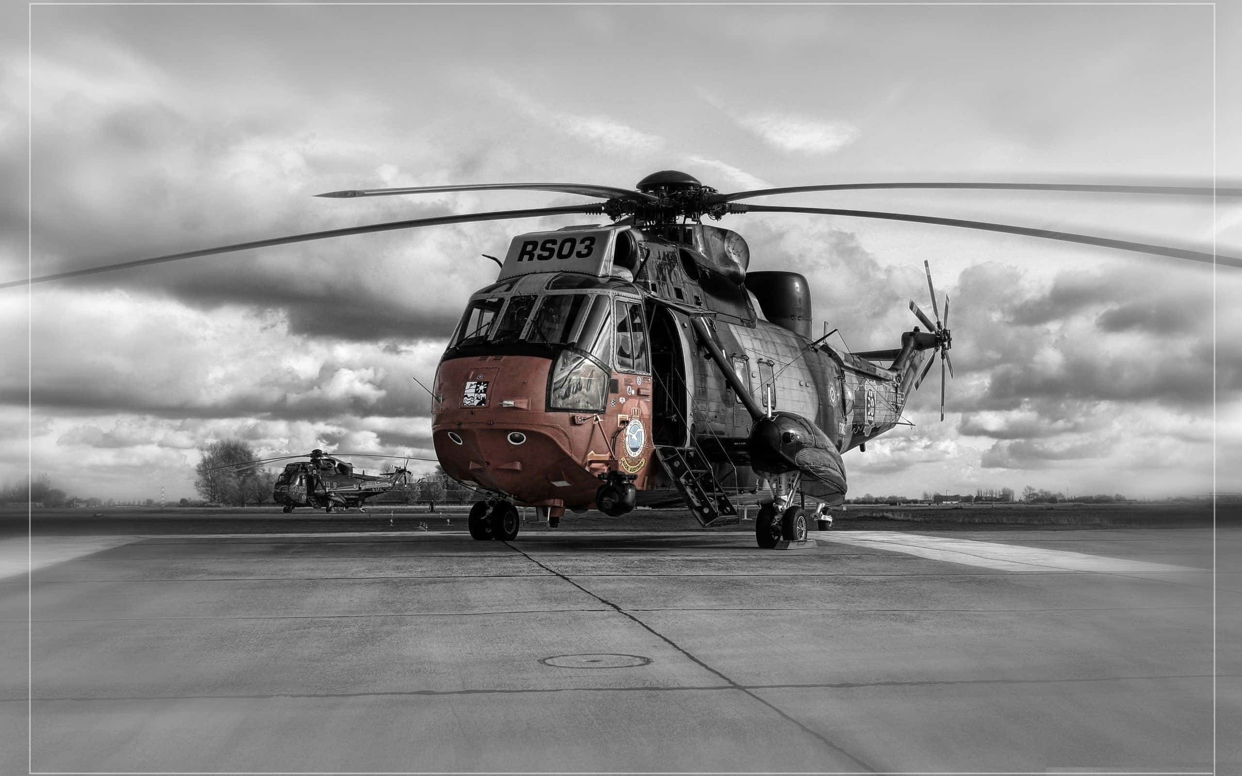 Helicopter 桌布 壁紙 — 一架紅色機頭、歷經風霜的軍用直升機停在停機坪上，背景是戲劇性的多雲天空，還有另一架直升機。